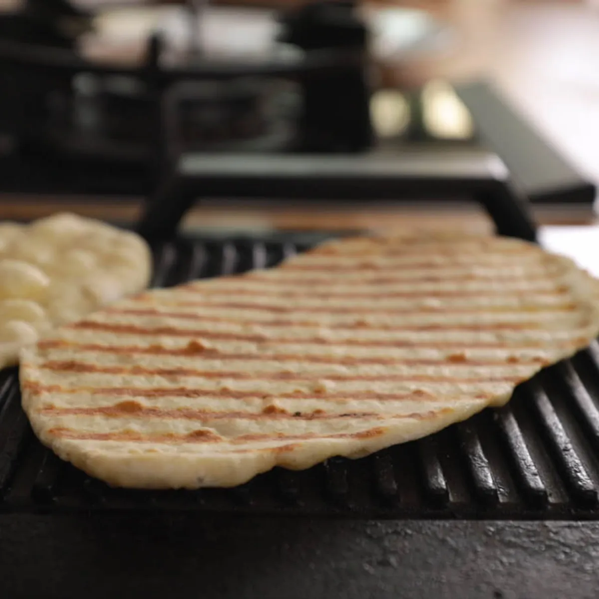 Two pieces of flatbread are cooking on a hot grill pan, one showing prominent grill marks.