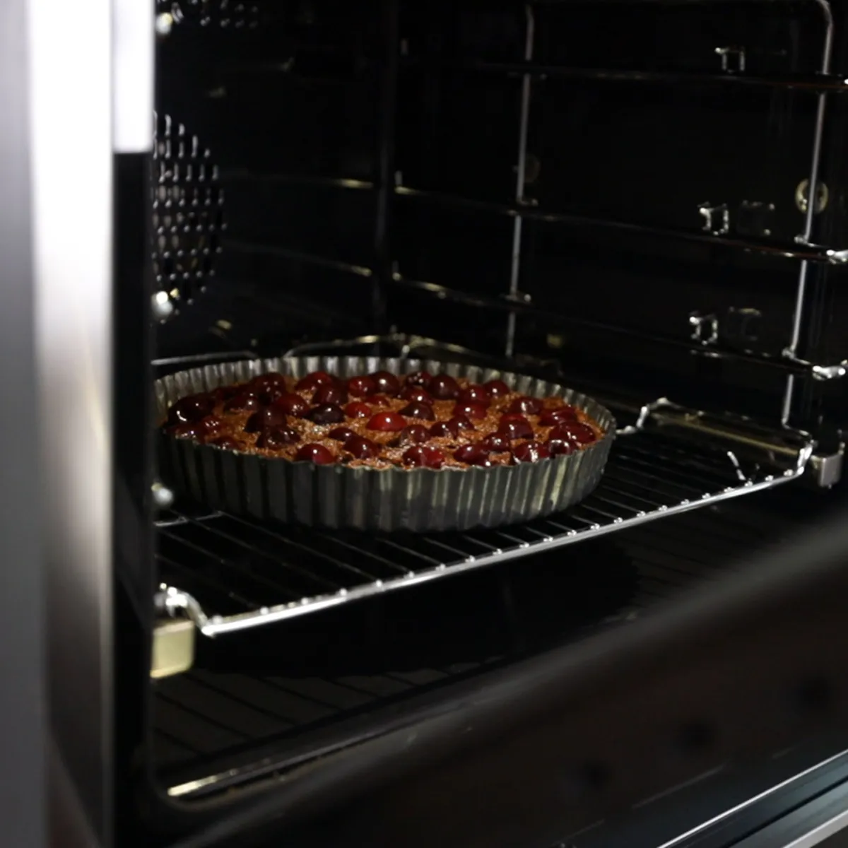 A fluted tart pan filled with a chocolate and cherry tart is placed into a hot oven.