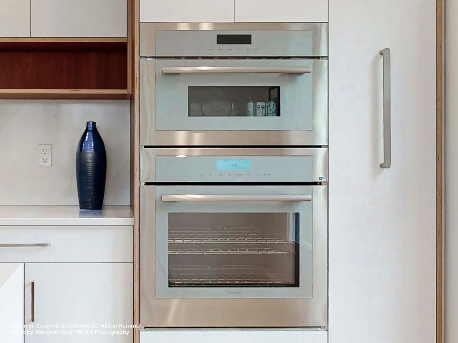 Stainless steel double oven built into a modern kitchen cabinet next to a blue vase.