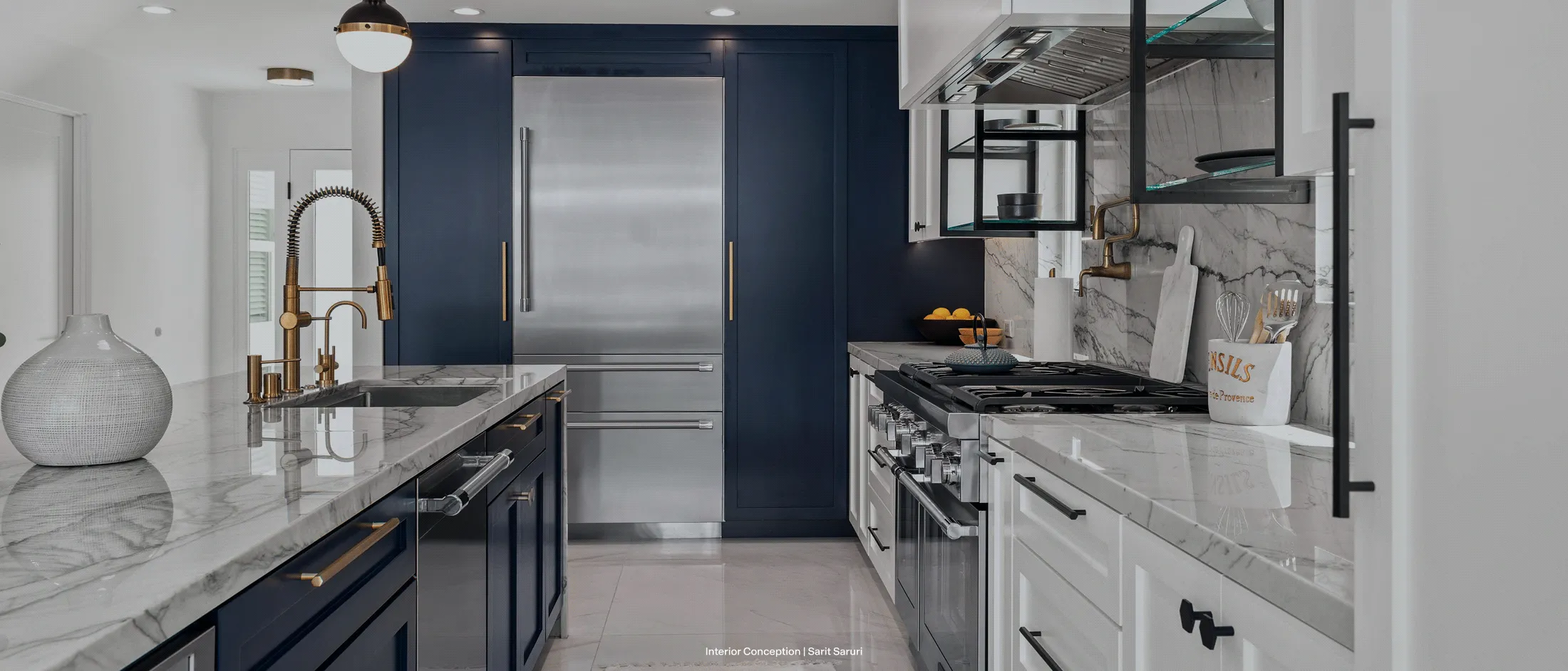 Modern kitchen with navy blue cabinets, marble countertops, gold fixtures, stainless steel appliances, and open shelving.