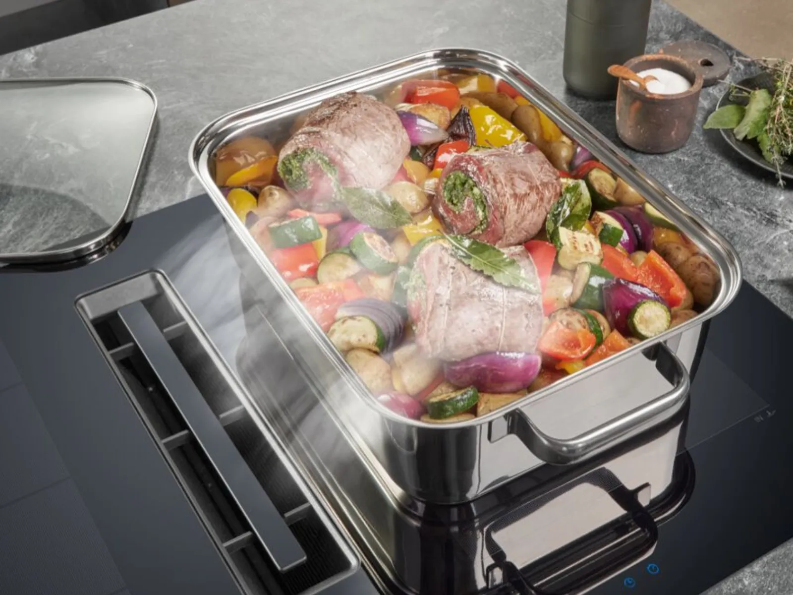 Rostat kött och grönsaker i en rostfri ugnsform på en modern induktionshäll.