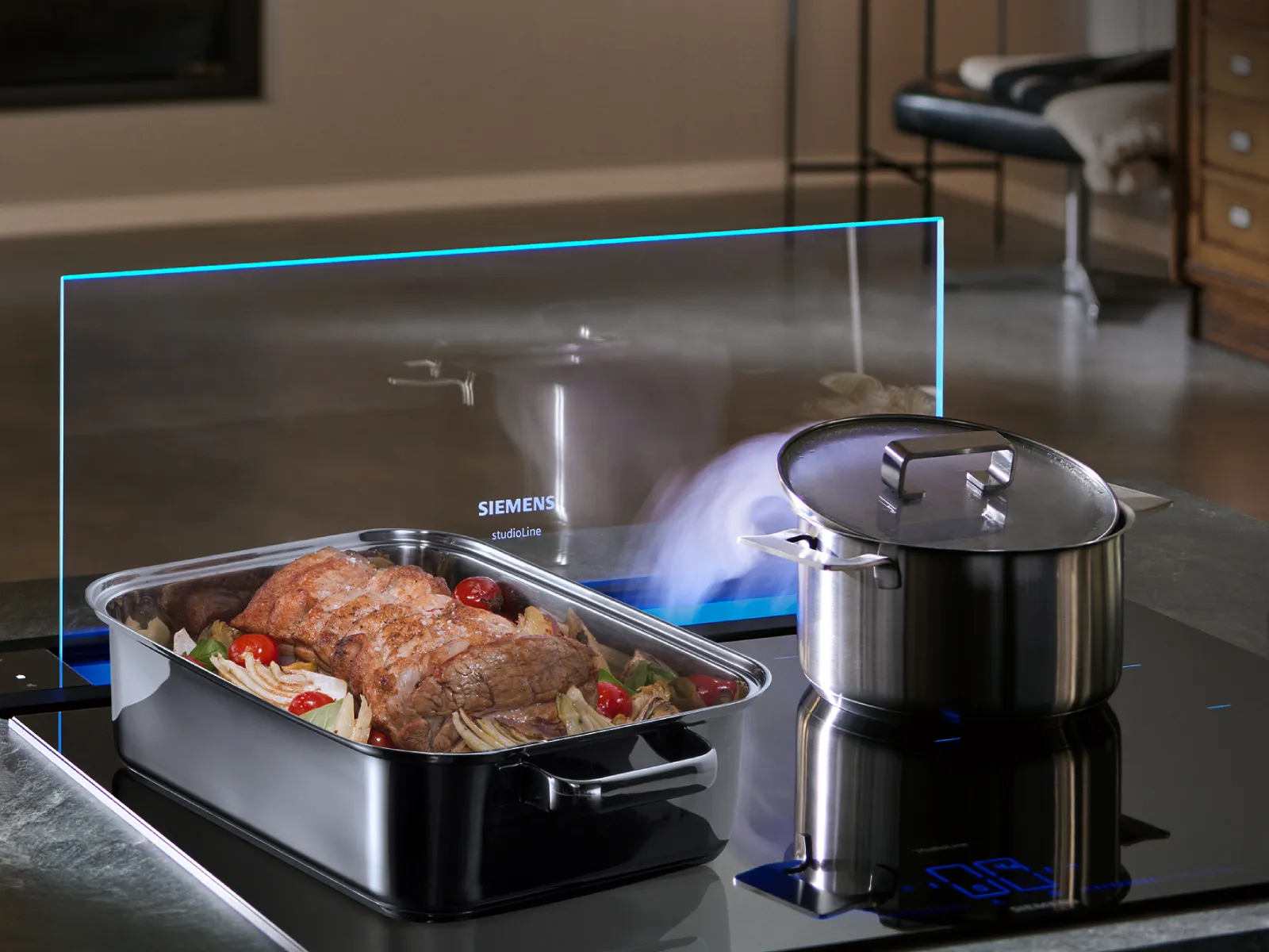 Ånga stiger från en gryta med lock på en svart induktionshäll, intill en ugnsform med tillagat kött och grönsaker och ett genomskinligt Siemens-stänkskydd.
