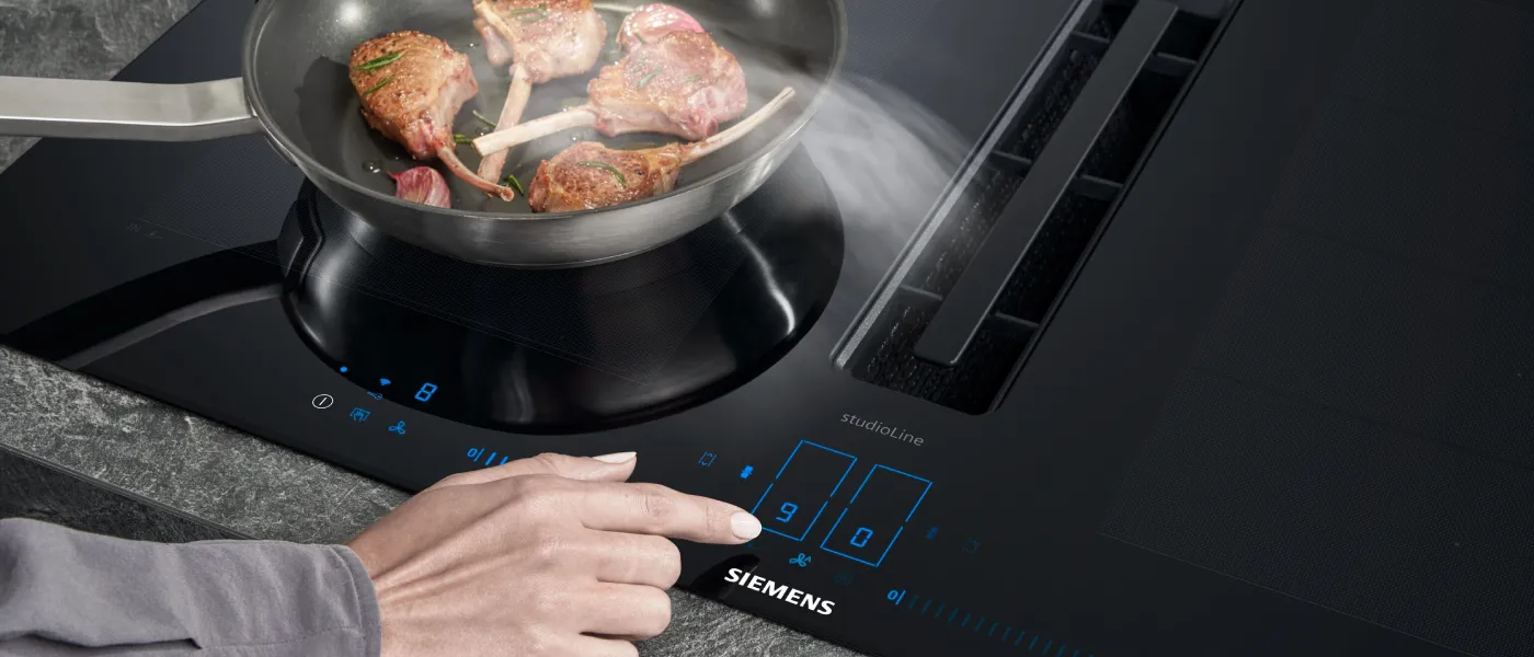 Händer som justerar spisreglage, lagar kött i en panna på en elektrisk spishäll.