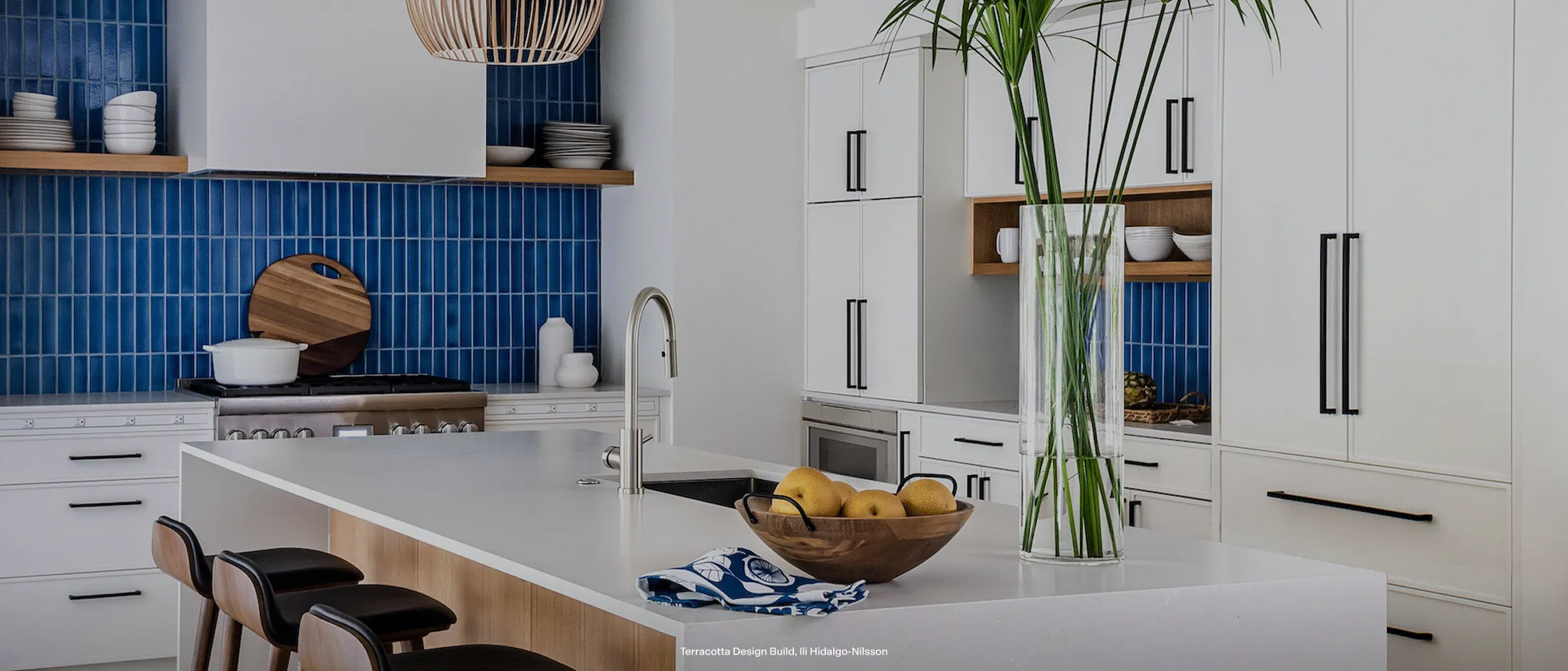 Modern kitchen with a white island, bold blue tile backsplash, and sleek white cabinetry.