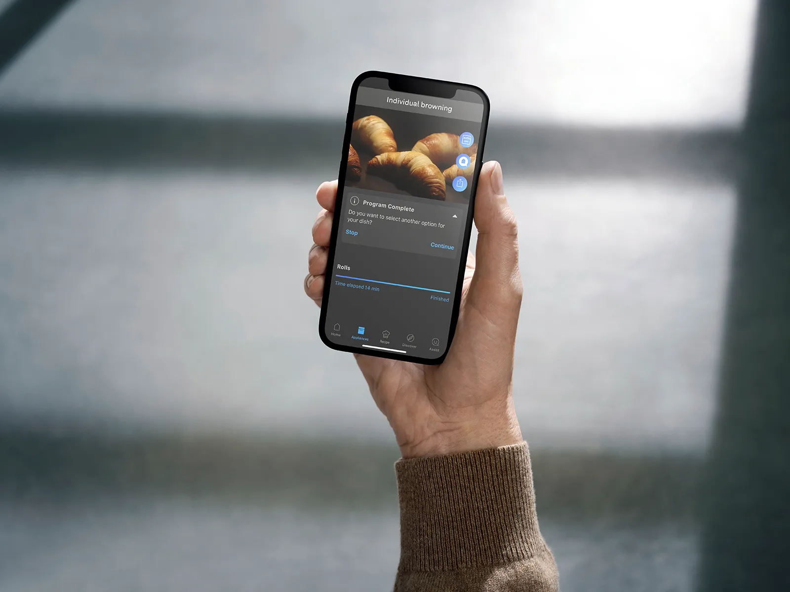 Smartphone displaying image of croissants, hand holding device against blurred background.