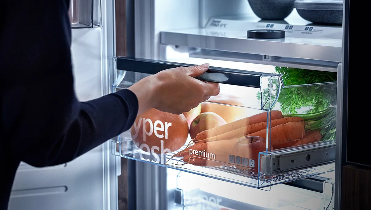 Open refrigerator with various food items, hand reaching for item.