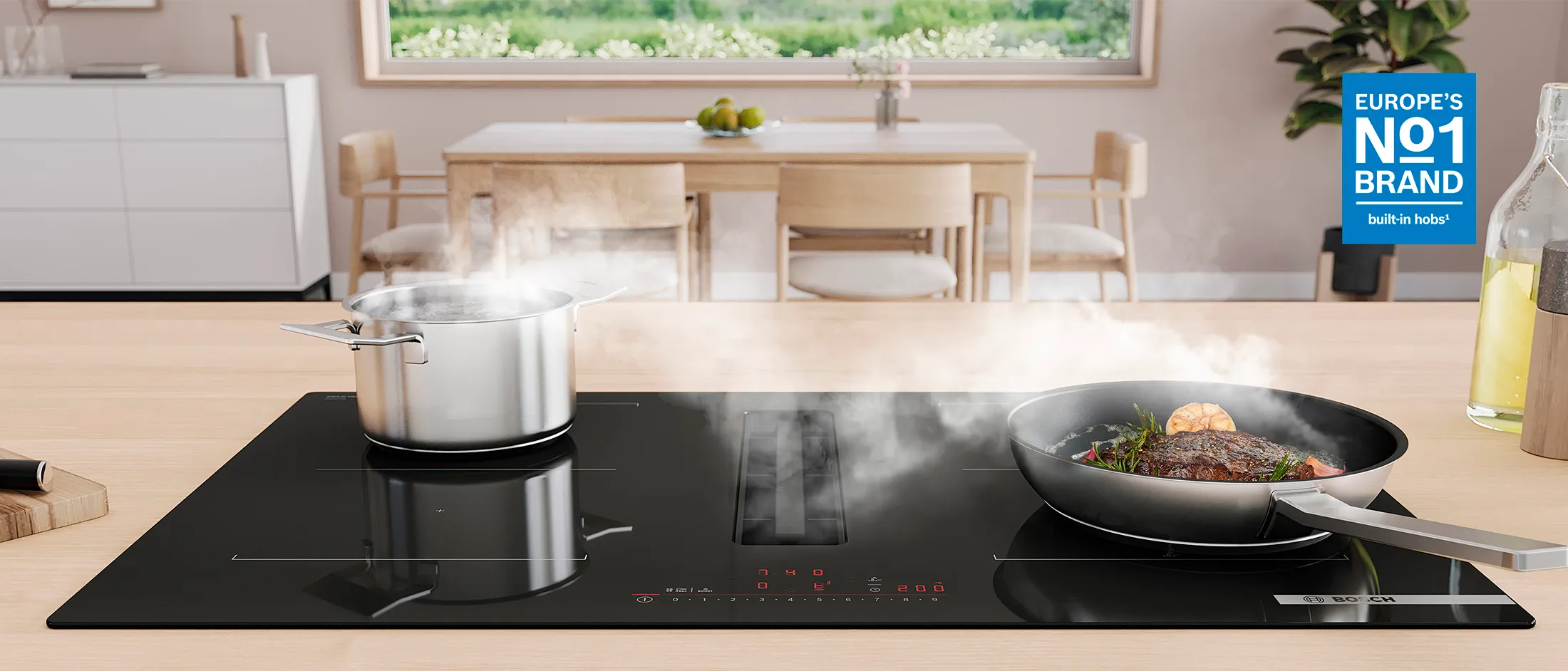 Cocina moderna con una encimera de inducción negra; una olla humeante y una sartén con comida cocinada, zona de comedor luminosa visible al fondo.