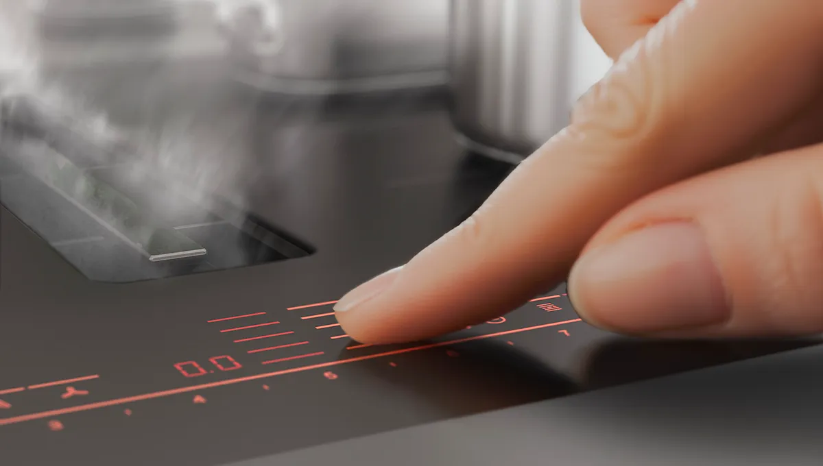 Un dedo ajustando el panel de control digital rojo en una encimera de inducción de cocina que emite vapor.