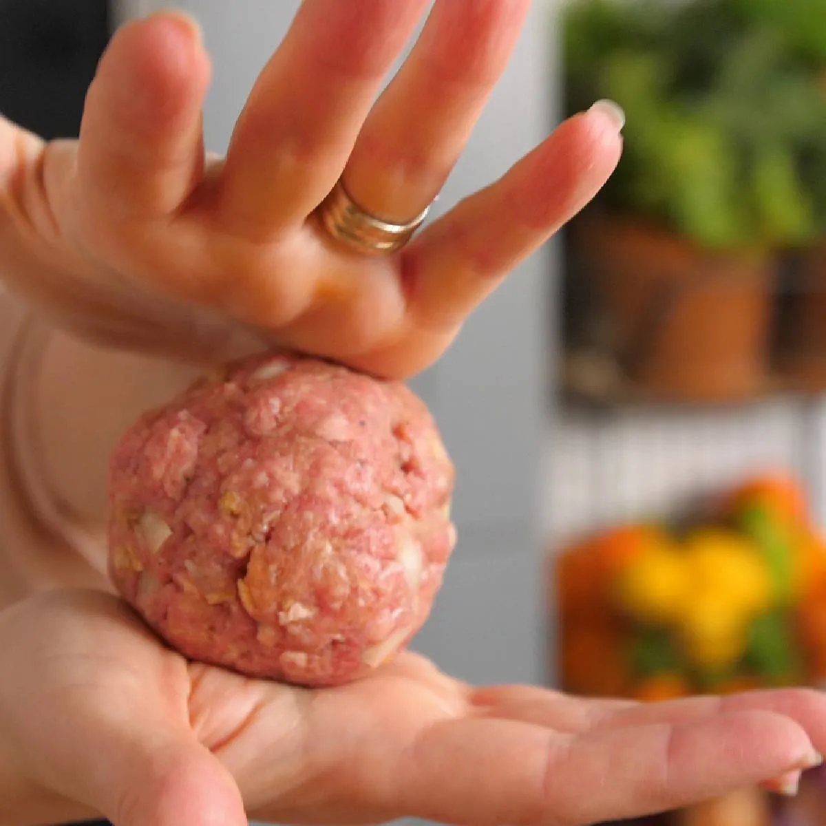 Hands shape a raw burger patty into a perfect round ball.