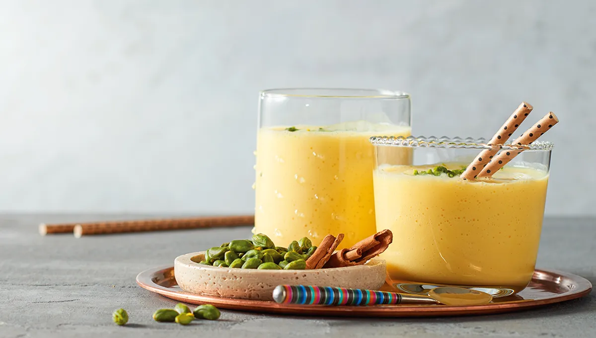 Due creme di colore giallo a base di albicocche riempite in bicchieri disposti insieme ad una piccola ciotola di pistacchi.