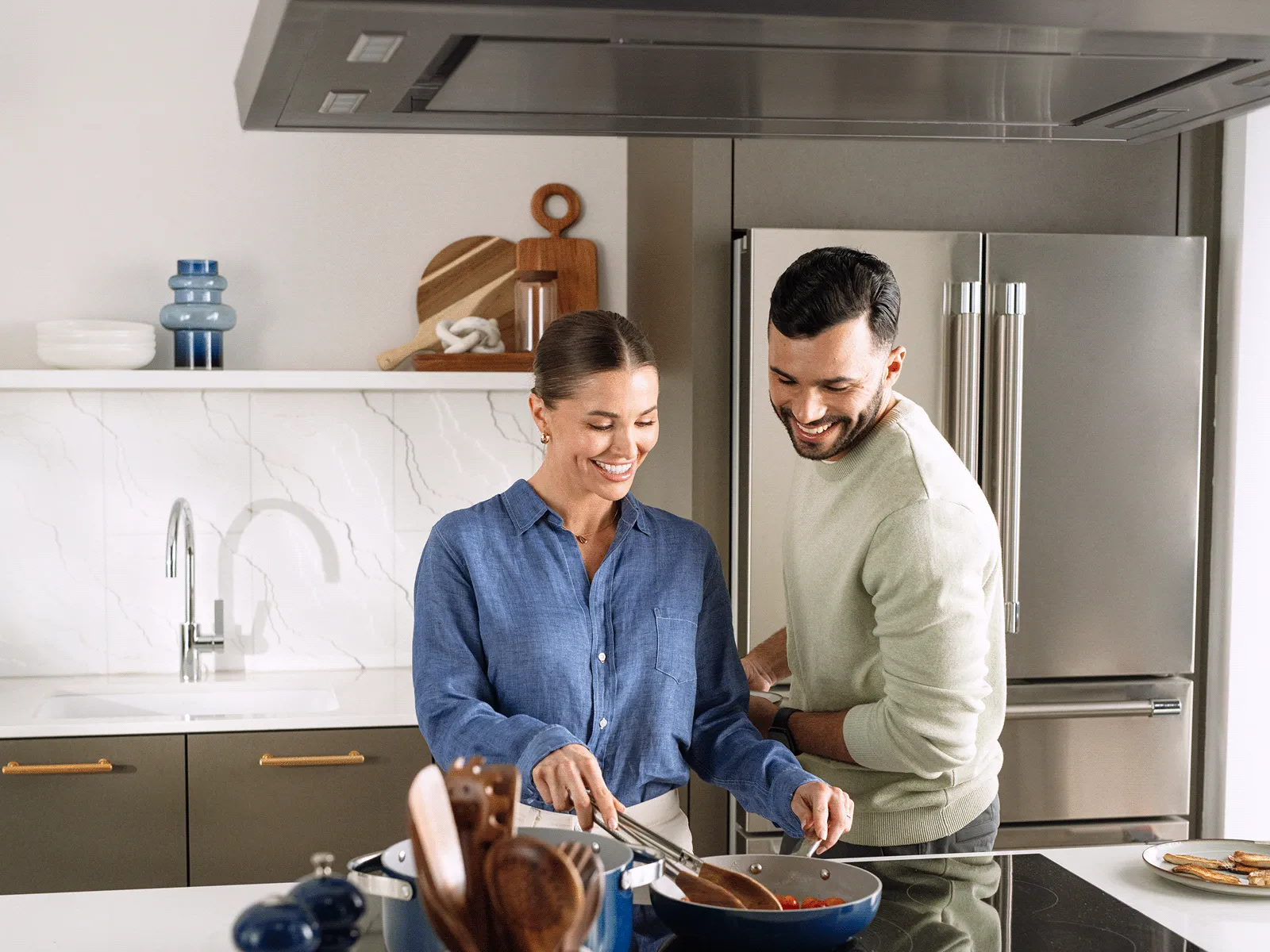 Un couple cuisine avec plaisir pendant que leur hotte îlot Thermador se synchronise avec la surface de cuisson.