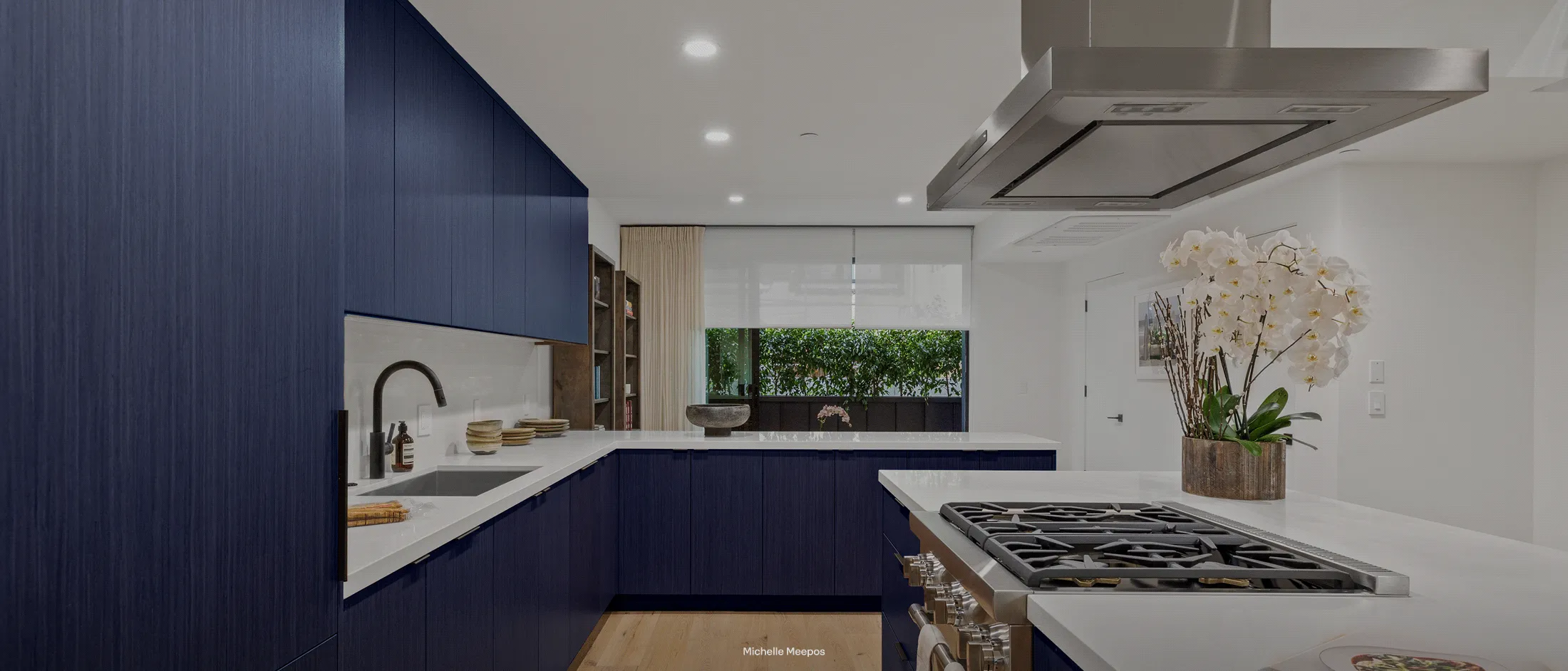 Wide shot of a stylish blue kitchen featuring a Thermador 36-inch island hood.