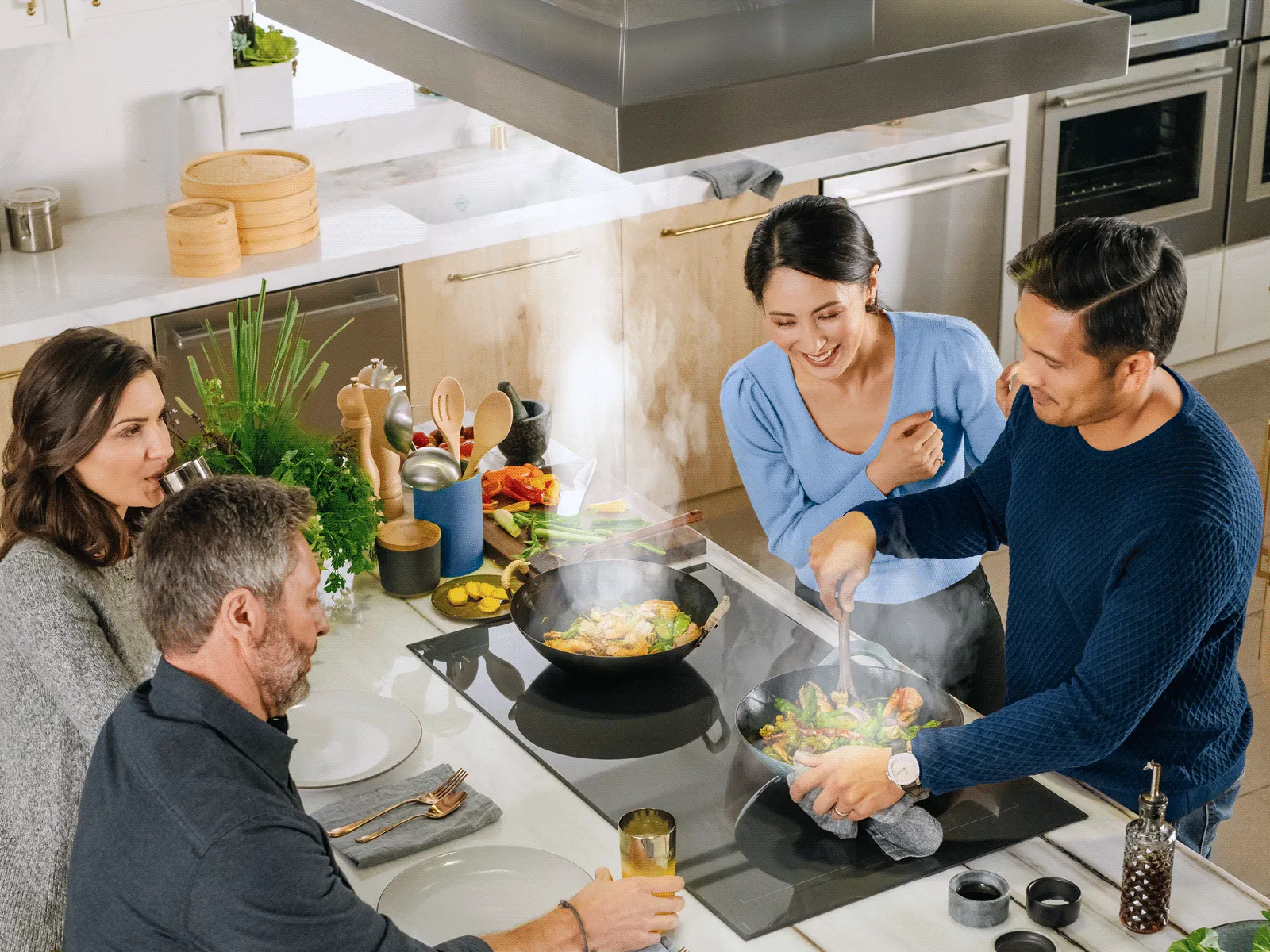 Group of people happily cooking and socializing under a large kitchen island hood.