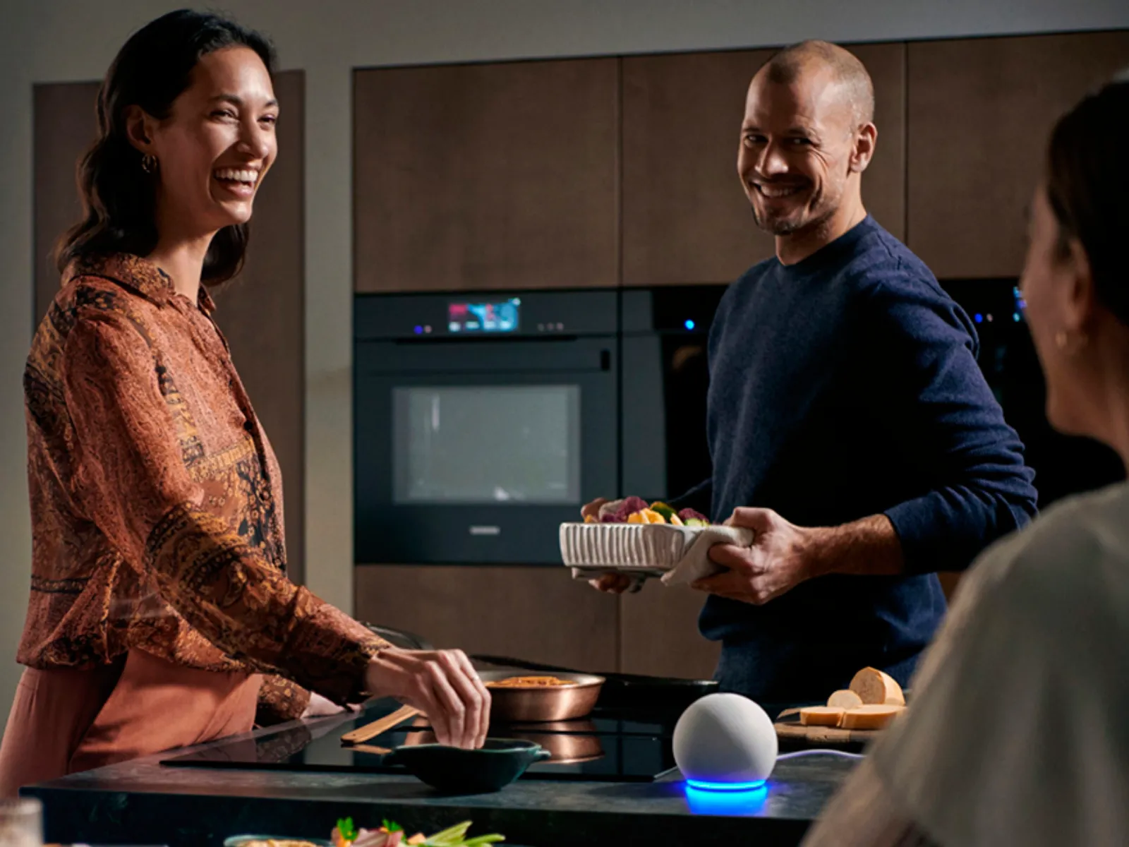 Happy people cooking in a modern kitchen with built-in Siemens appliances and a smart speaker.