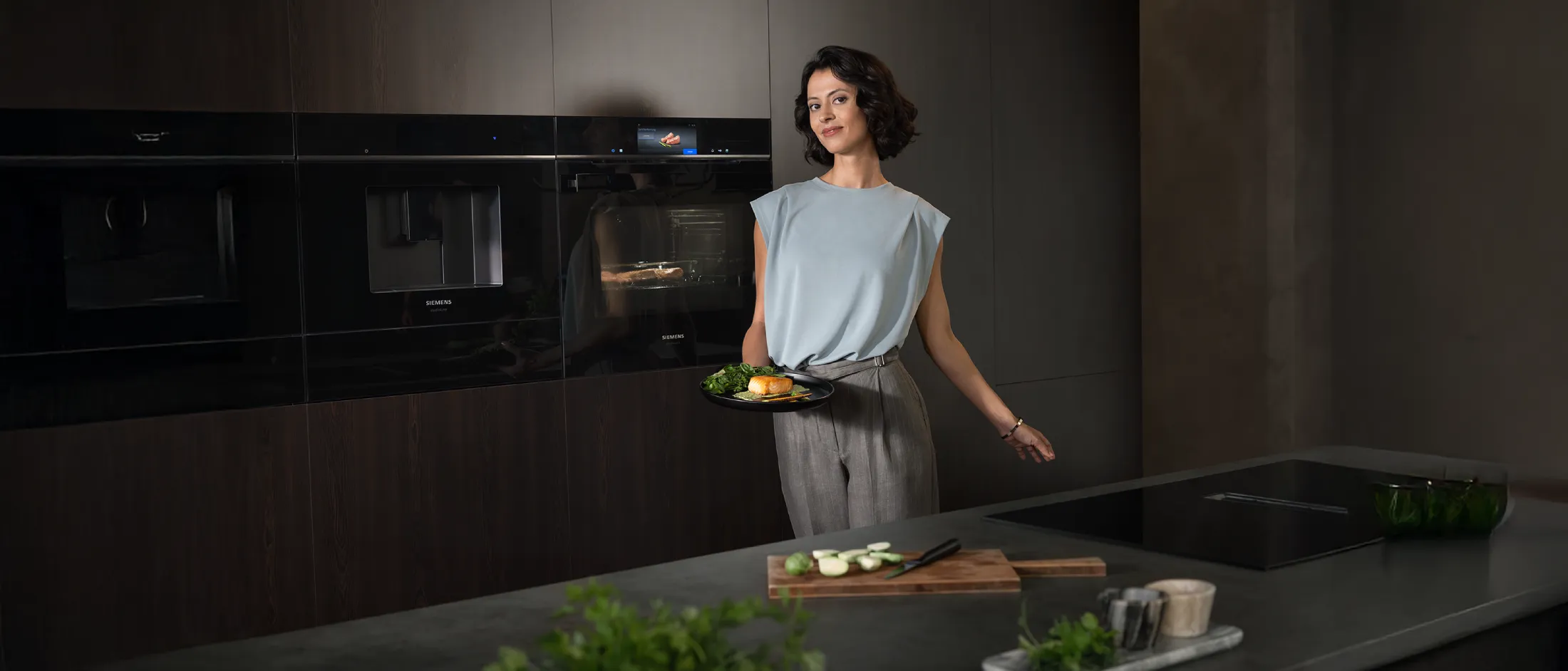 A stylish kitchen scene with a person holding a plate of food, surrounded by sleek appliances and a modern countertop.