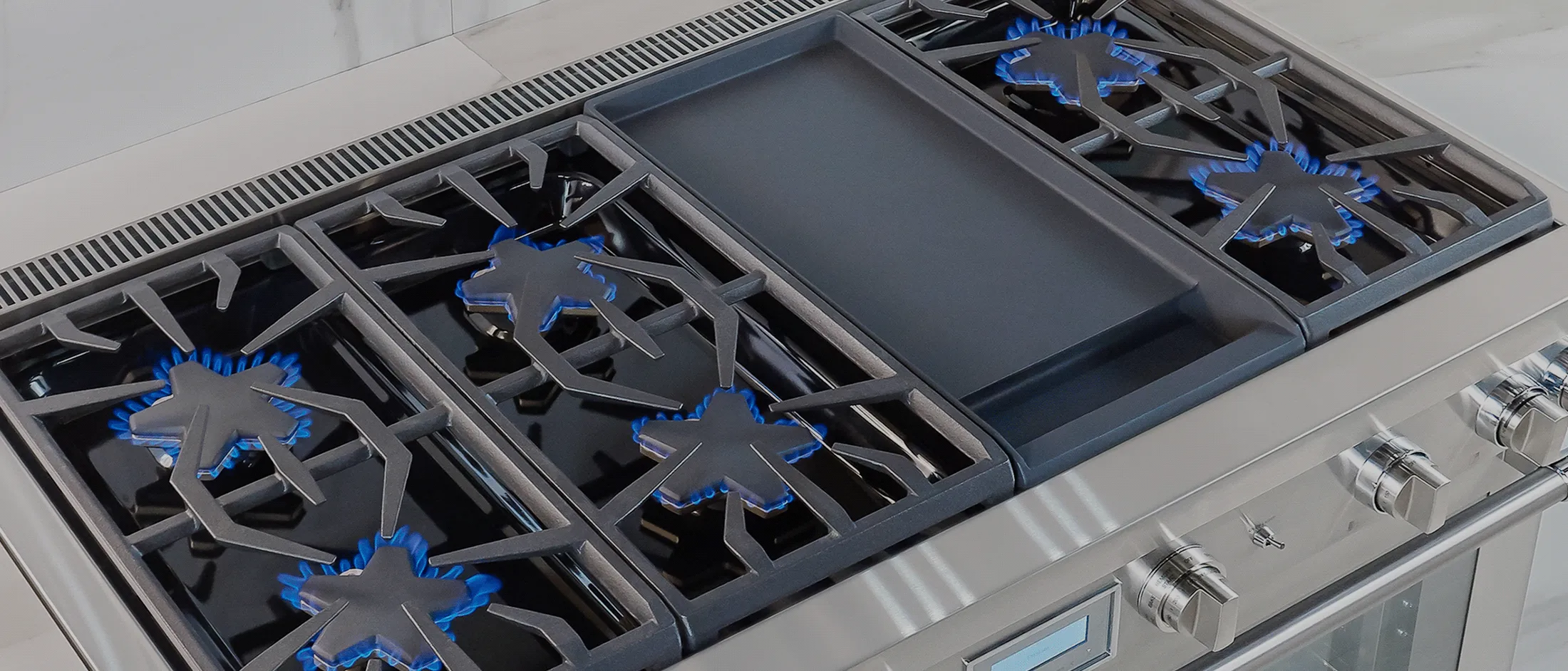 Stainless steel gas stove with six burners and two griddle plates in a modern kitchen setting.