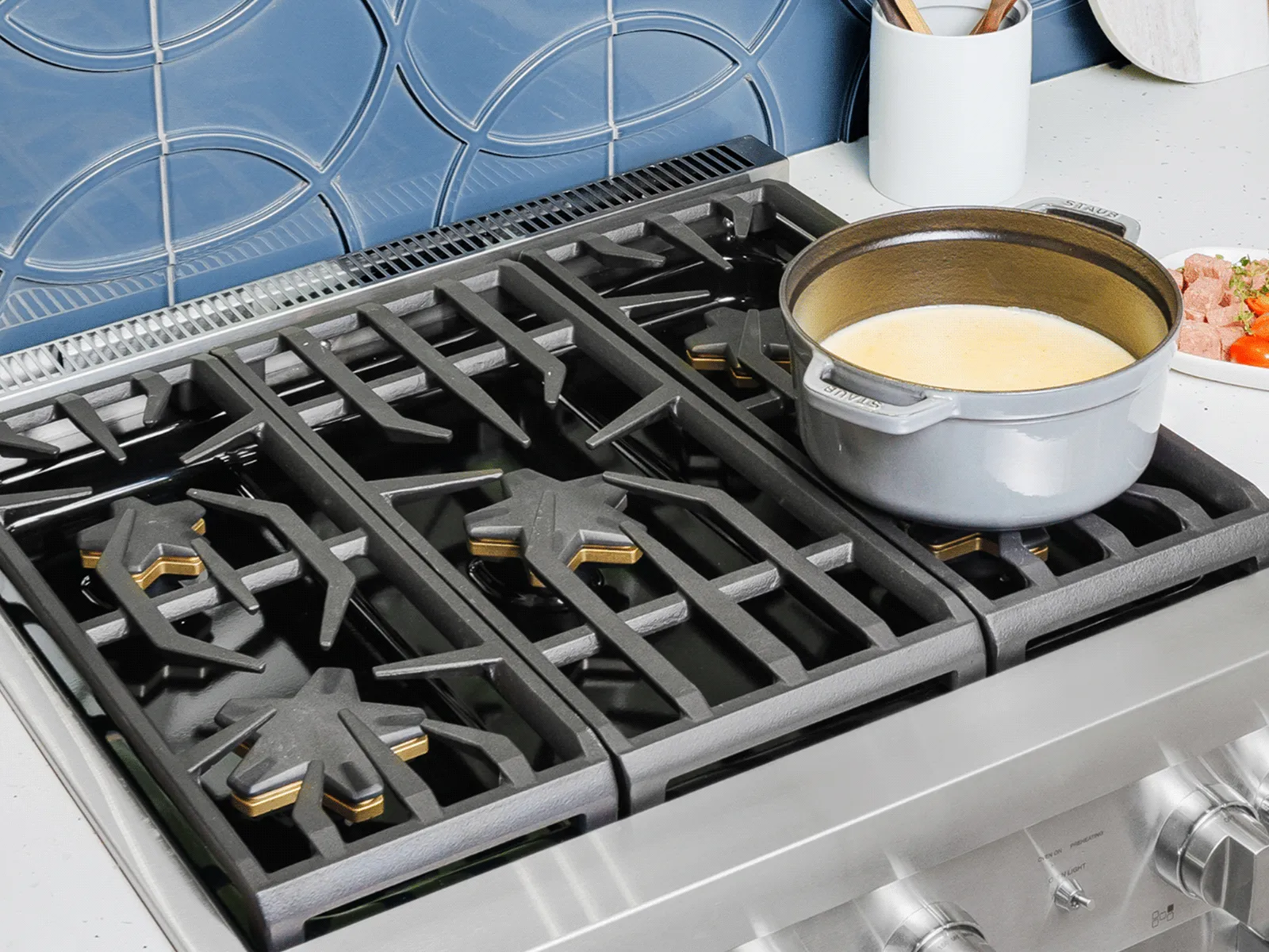 Silver pot with creamy soup simmering on a modern stainless steel gas stove in a kitchen with blue tiled backsplash.