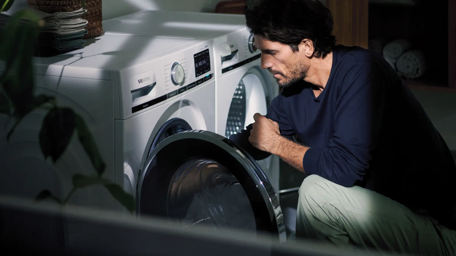 Uomo che guarda all'interno di una lavatrice Siemens, con un'asciugatrice coordinata posizionata a fianco.