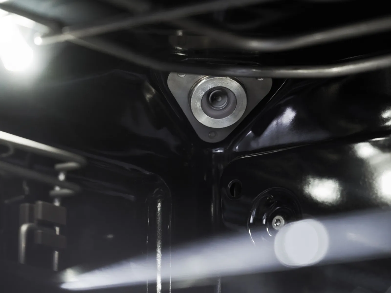 Metallic camera lens or sensor mounted inside a dark, glossy appliance interior, with light reflections.