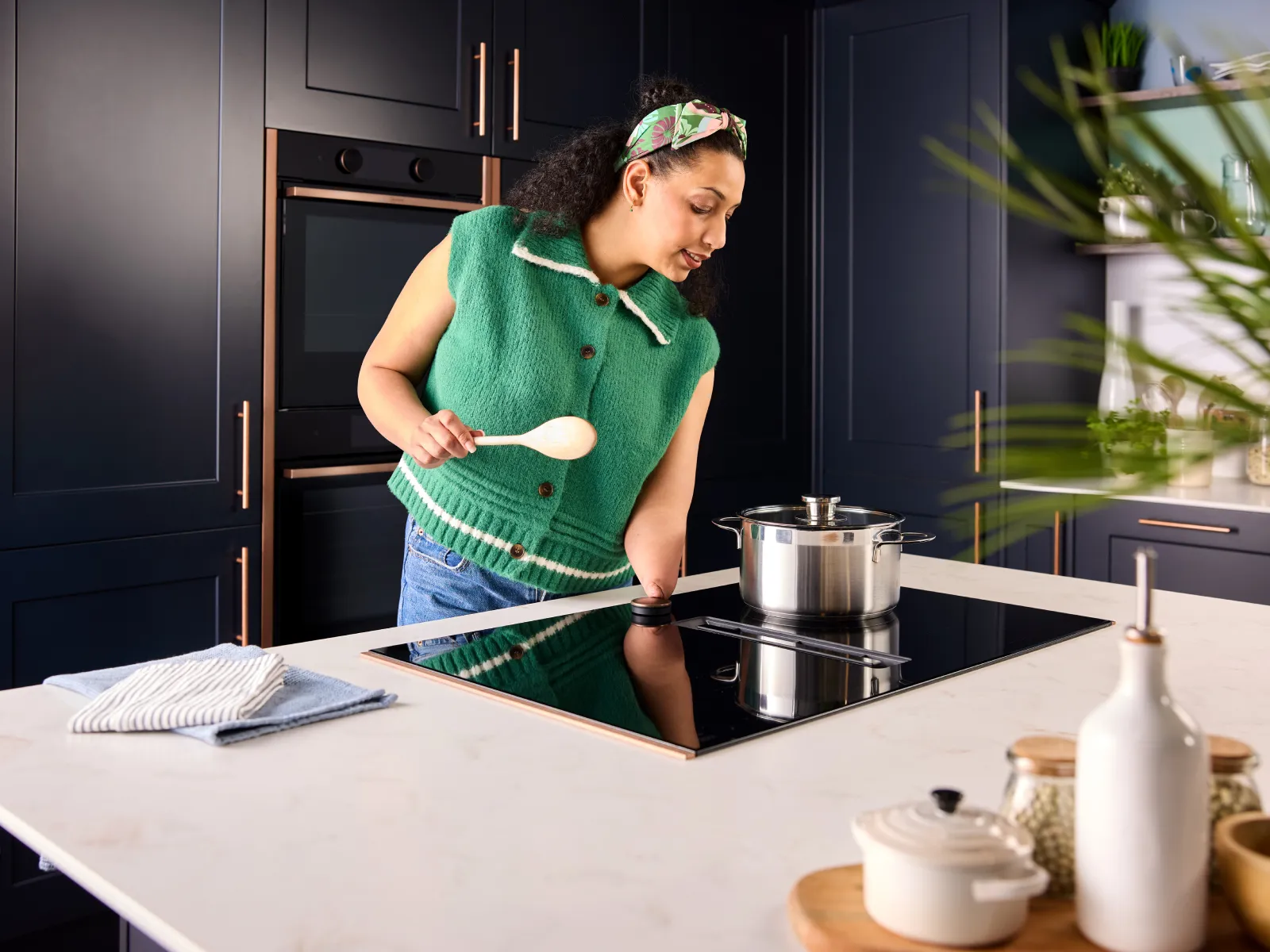 A woman with a limb difference stands at an induction hob. She lightly touches the magnetic dial to adjust the pan temperature.