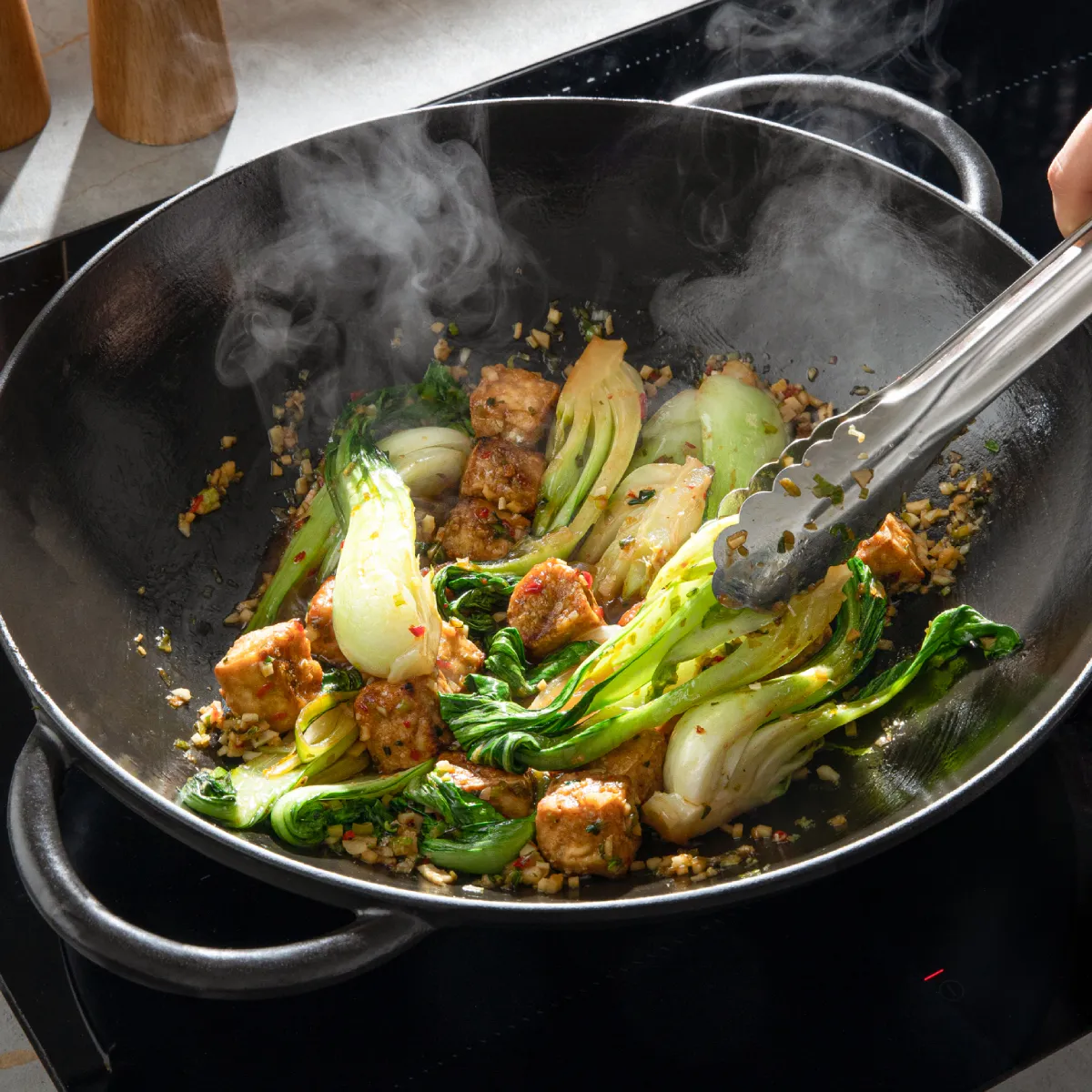 Sizzling wok with steaming vegetables, meat, and spices on a kitchen counter.