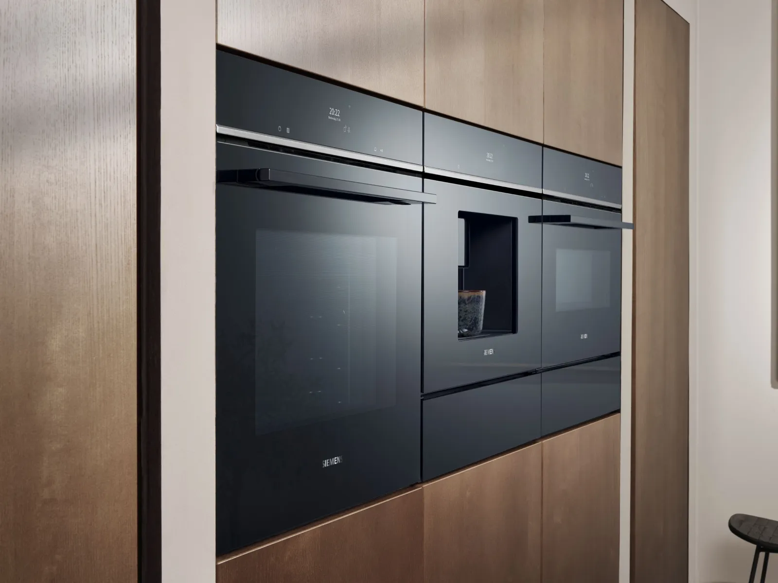 Des appareils électroménagers Siemens encastrés en verre noir intégrés dans des meubles en bois au cœur d’une cuisine moderne.