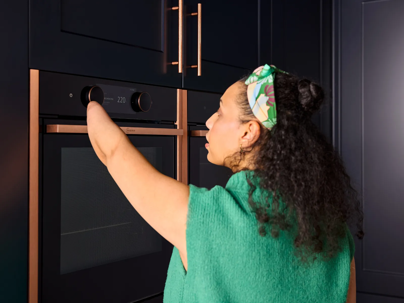Behind shot of a woman with a limb difference affecting one forearm, using her arm to adjust the oven controls on the slide and hide oven.