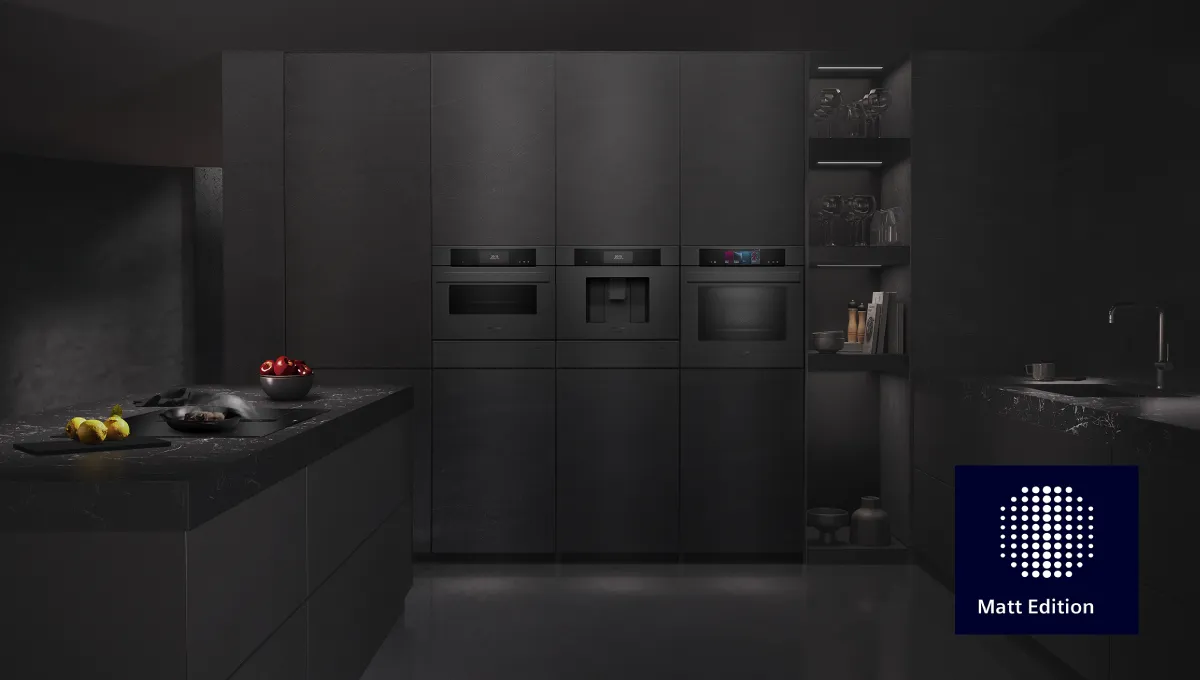 Dark, modern kitchen with matte black integrated appliances and cabinetry. Cooking island with food. Matt Edition logo.