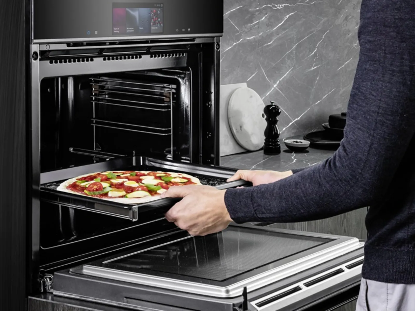 Un‘immagine mostra un uomo che regge una teglia di pizza con entrambe le mani, pronto a inserirla in un forno da incasso Siemens iQ700.