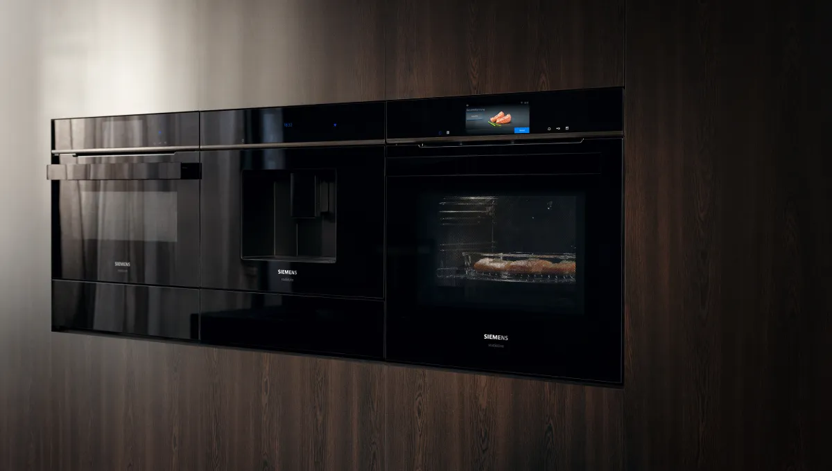 Built-in Siemens kitchen appliances: microwave, coffee machine, and oven cooking food, integrated into dark wood.