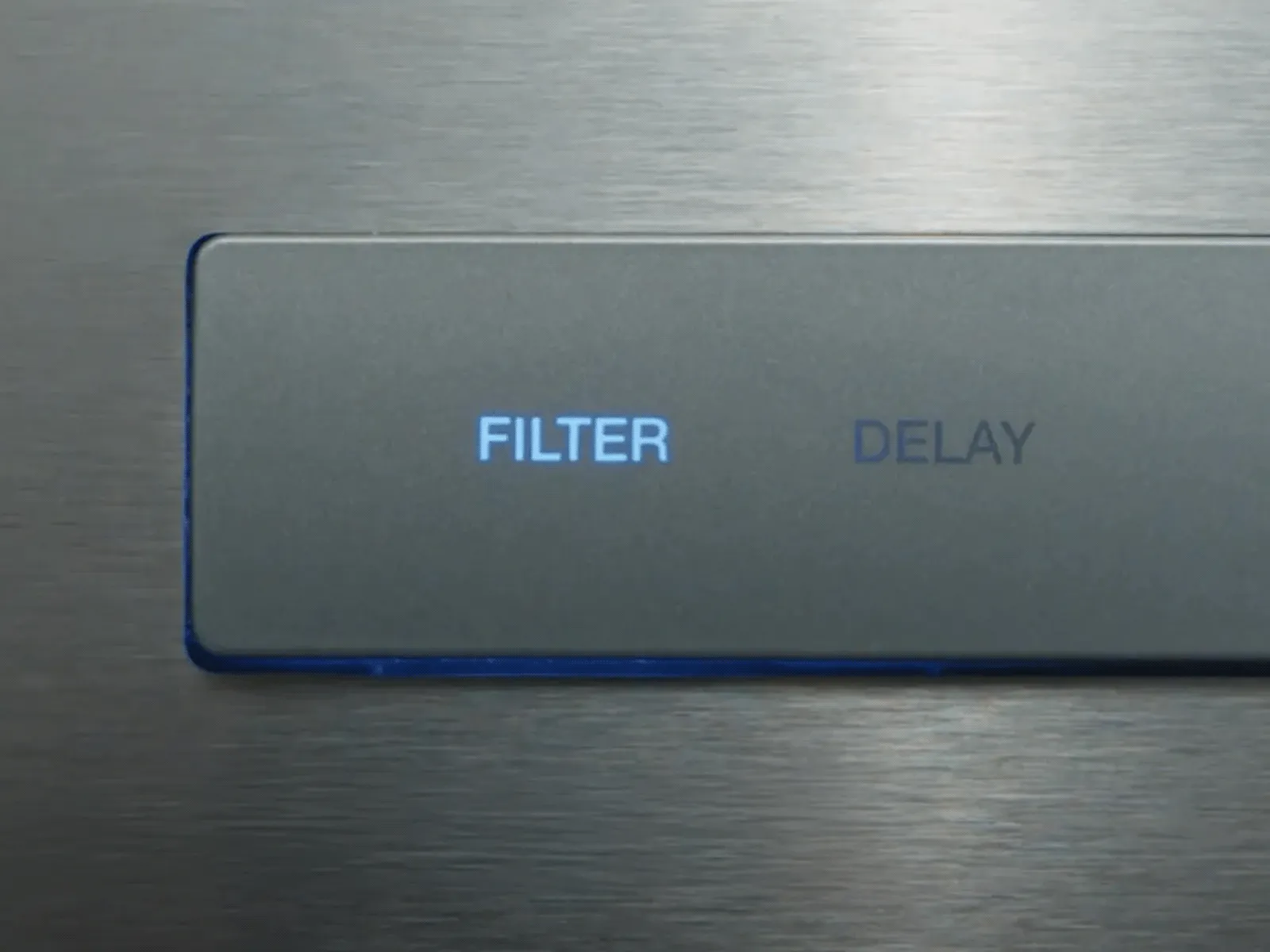 Close-up of a control panel with illuminated "FILTER" button and a dim "DELAY" label on a metallic surface.