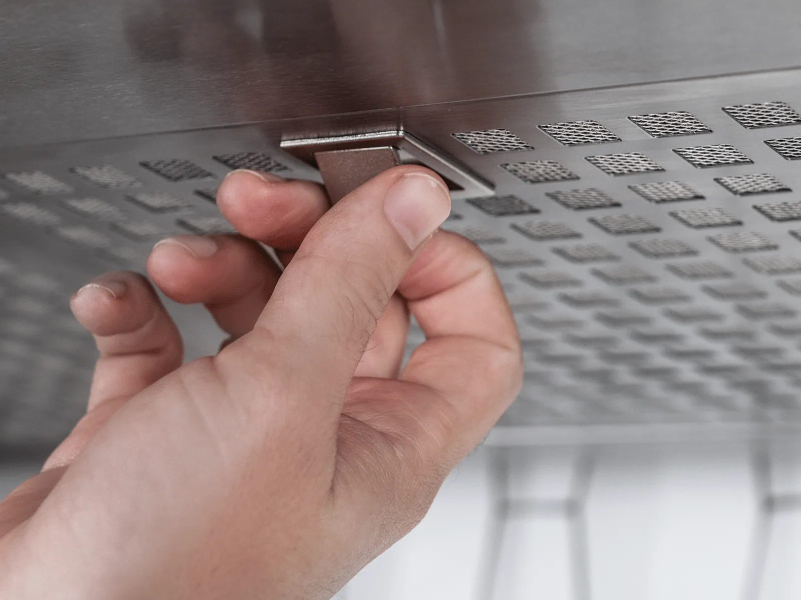 Hand pressing a button on a stainless steel panel with ventilation holes, likely part of an appliance or machine.