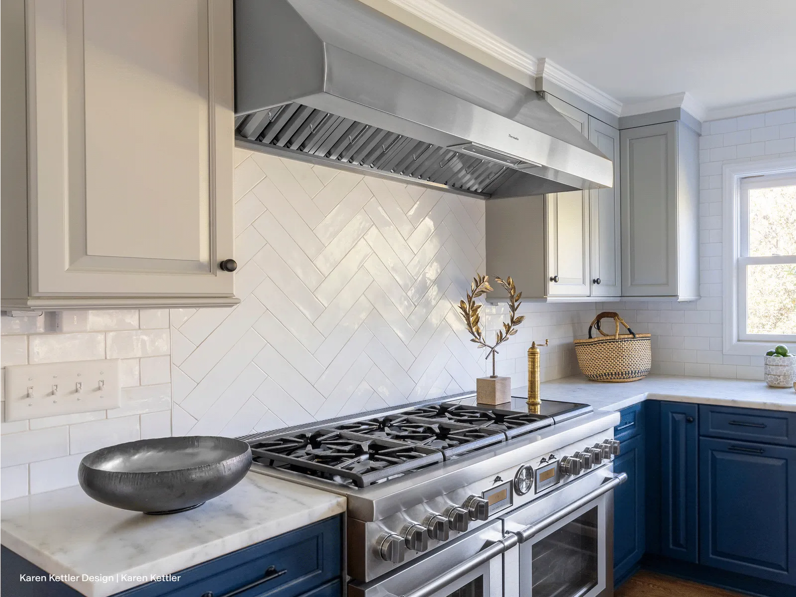 Modern kitchen with stainless steel gas range and hood, white tile backsplash, blue lower cabinets, and marble countertops.