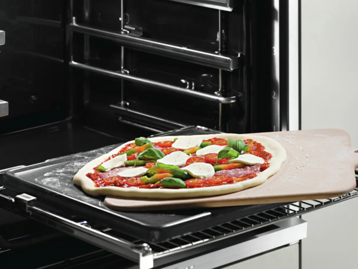 A person carefully removes a freshly baked pizza from the oven, showcasing its golden crust and melted cheese.
