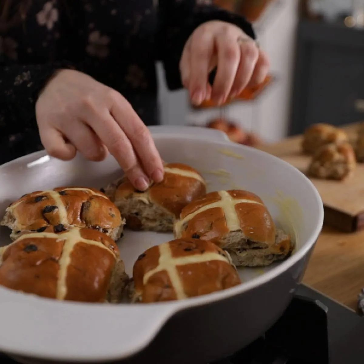Person arranging hot cross buns in baking dish