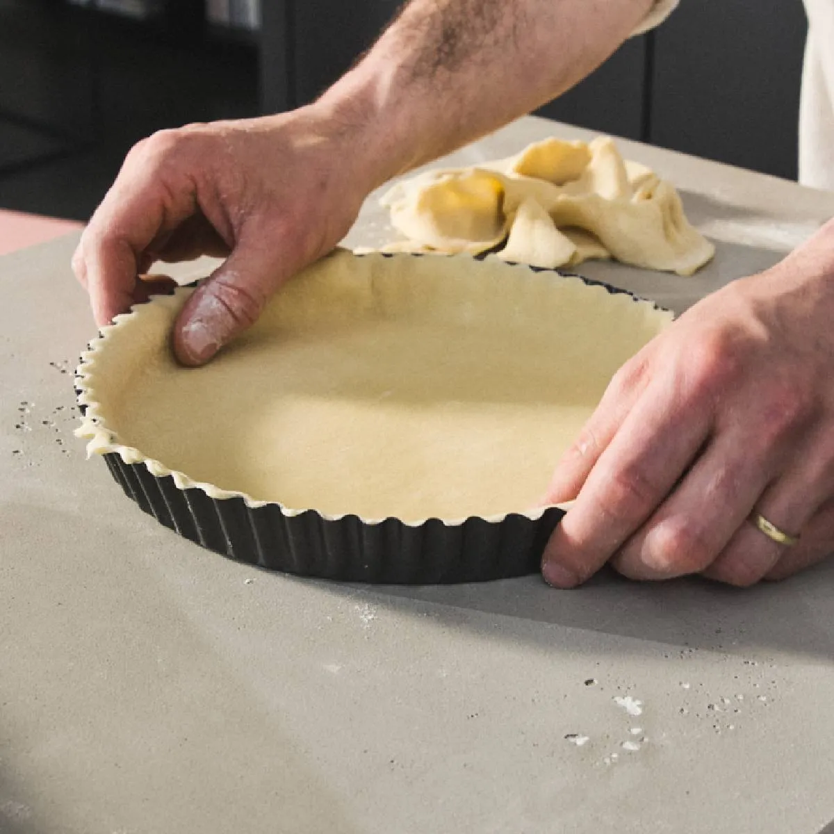 Hands preparing a pastry crust in a kitchen setting.