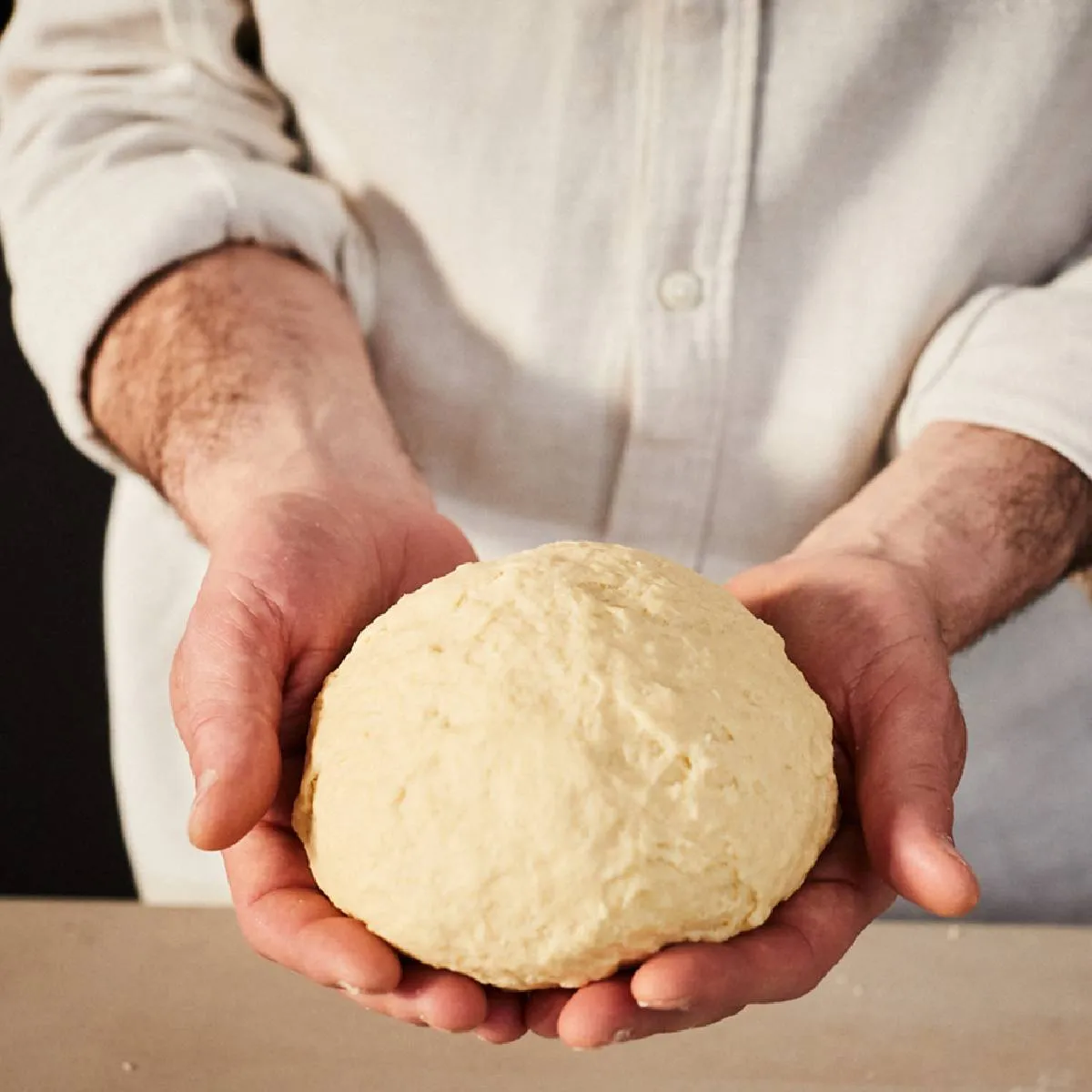 Chef's hands holding freshly kneaded dough on wooden surface.