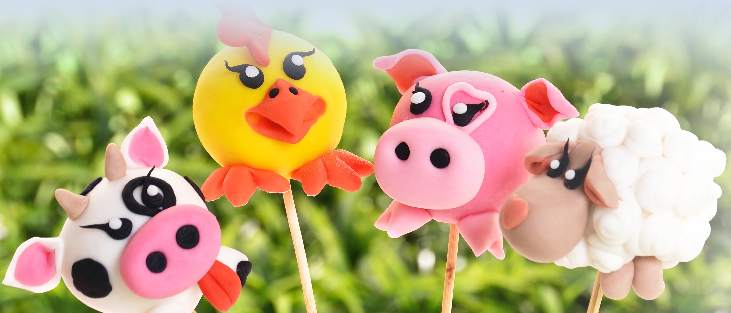 Vier bunte Cake-Pops in Form von Tierköpfen: eine Kuh, ein Huhn, ein Schwein und ein Schaf.