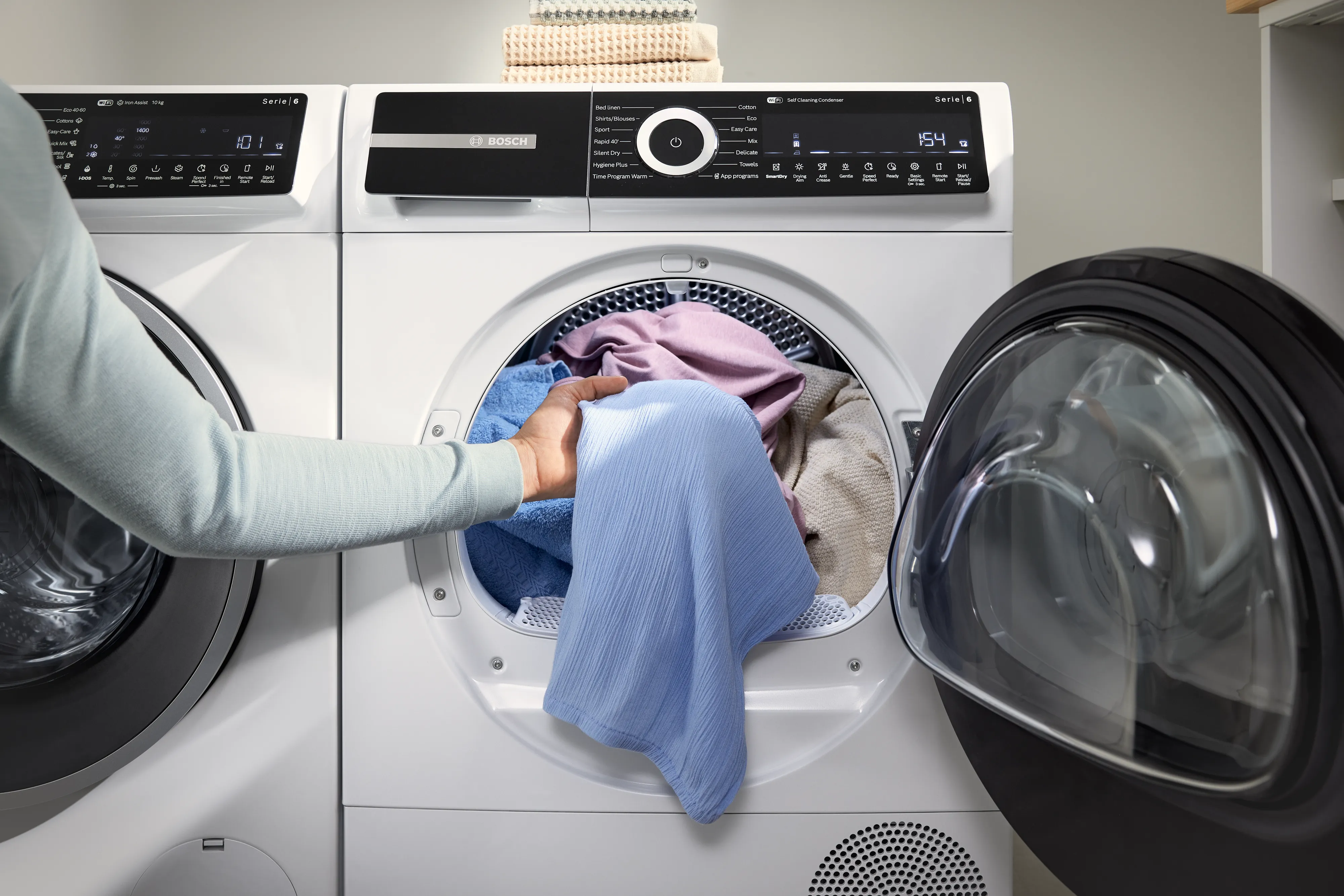 Main retirant un vêtement bleu clair d'un sèche-linge blanc à porte ronde ouverte