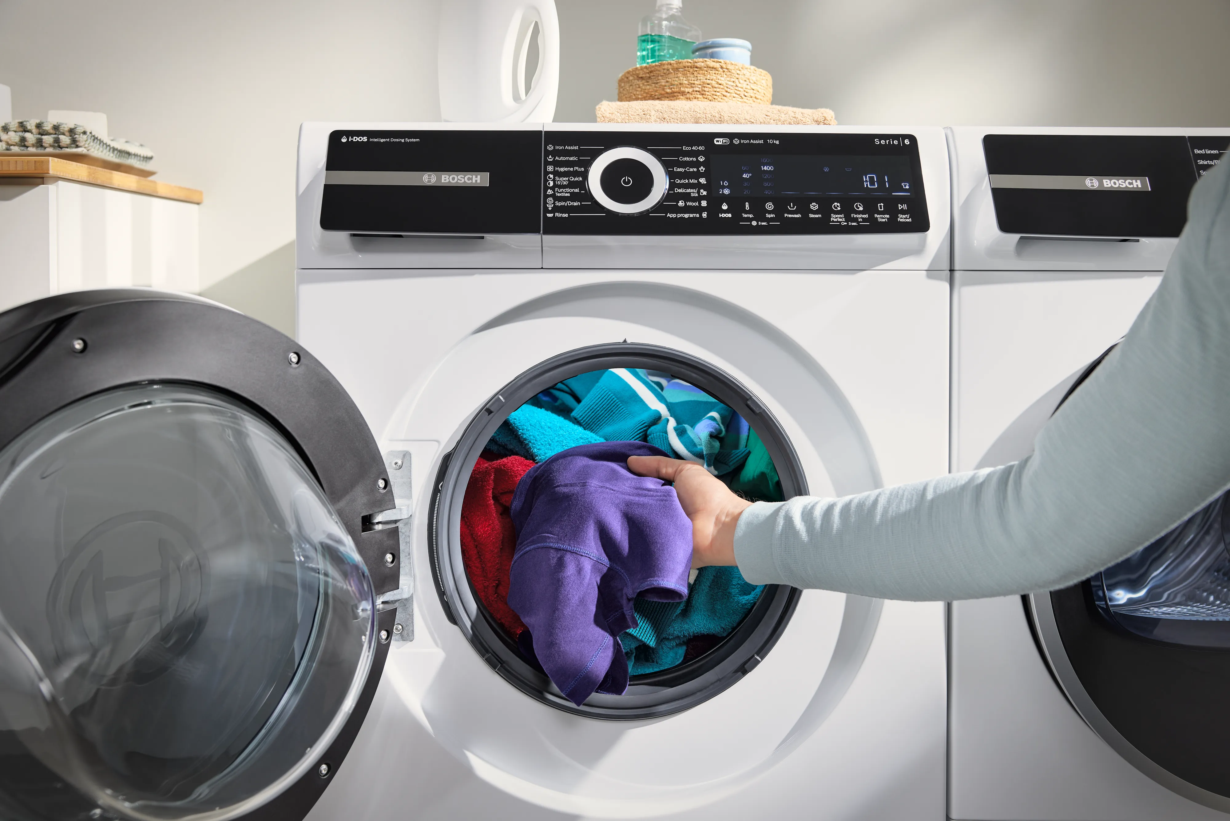 Hand die kleurrijke kleding in een voorlader-wasmachine stopt