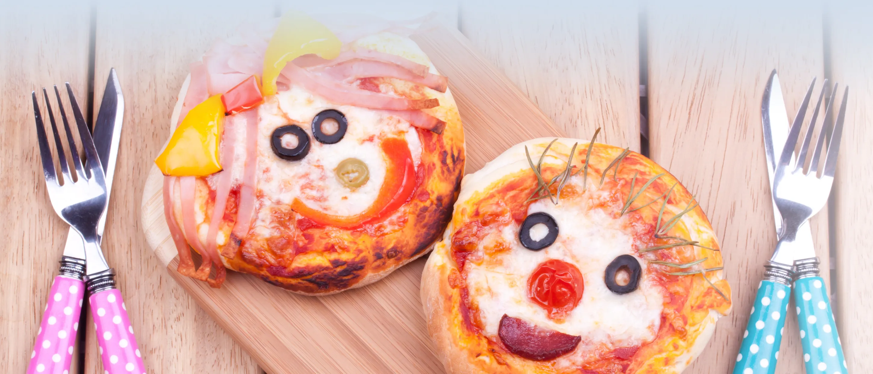 Zwei kleine Pizzen, die als lustige Gesichter mit Gemüse und Schinken dekoriert sind.
