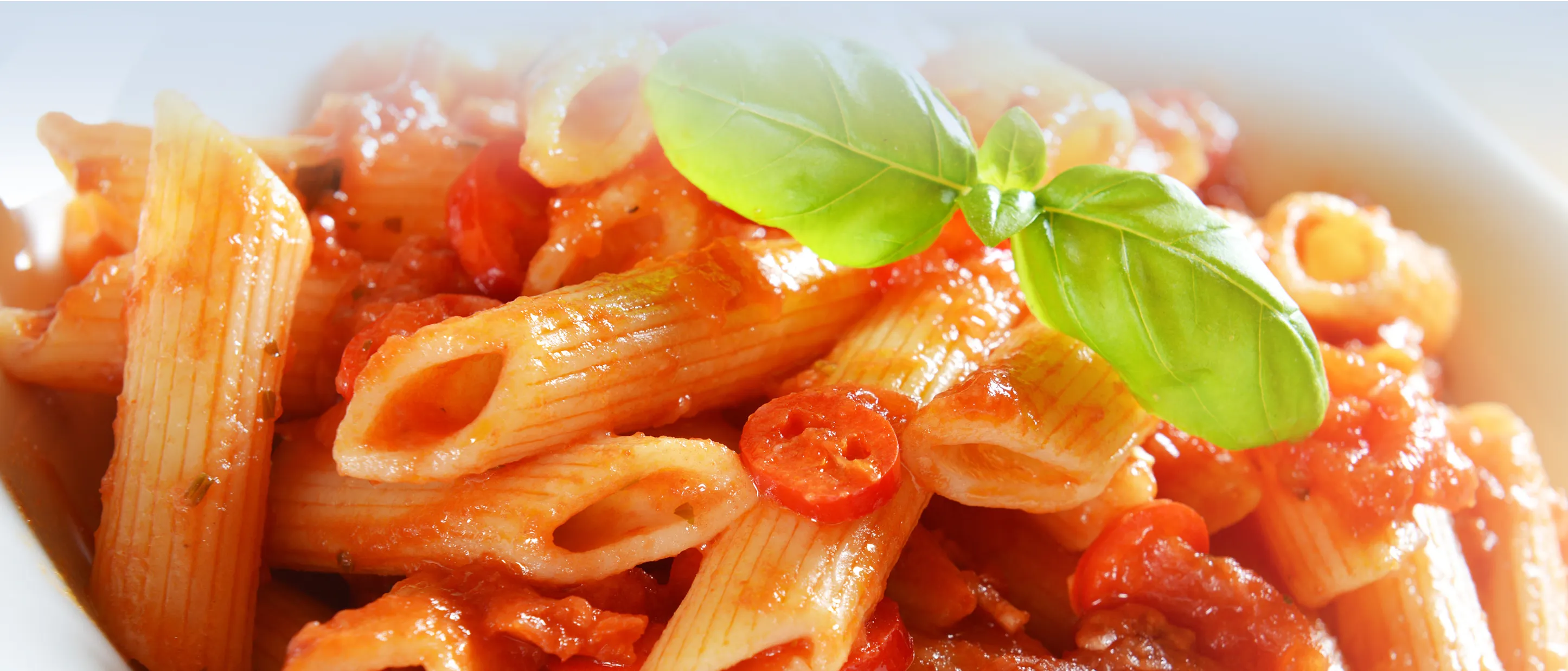 Nahaufnahme von Penne in Tomatensauce, garniert mit einem frischen Basilikumblatt