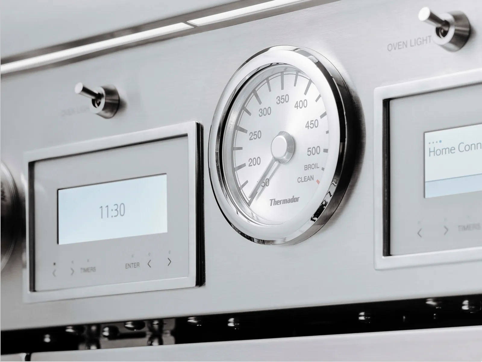 Close-up of stainless-steel oven controls with analog temperature gauge and two digital displays.