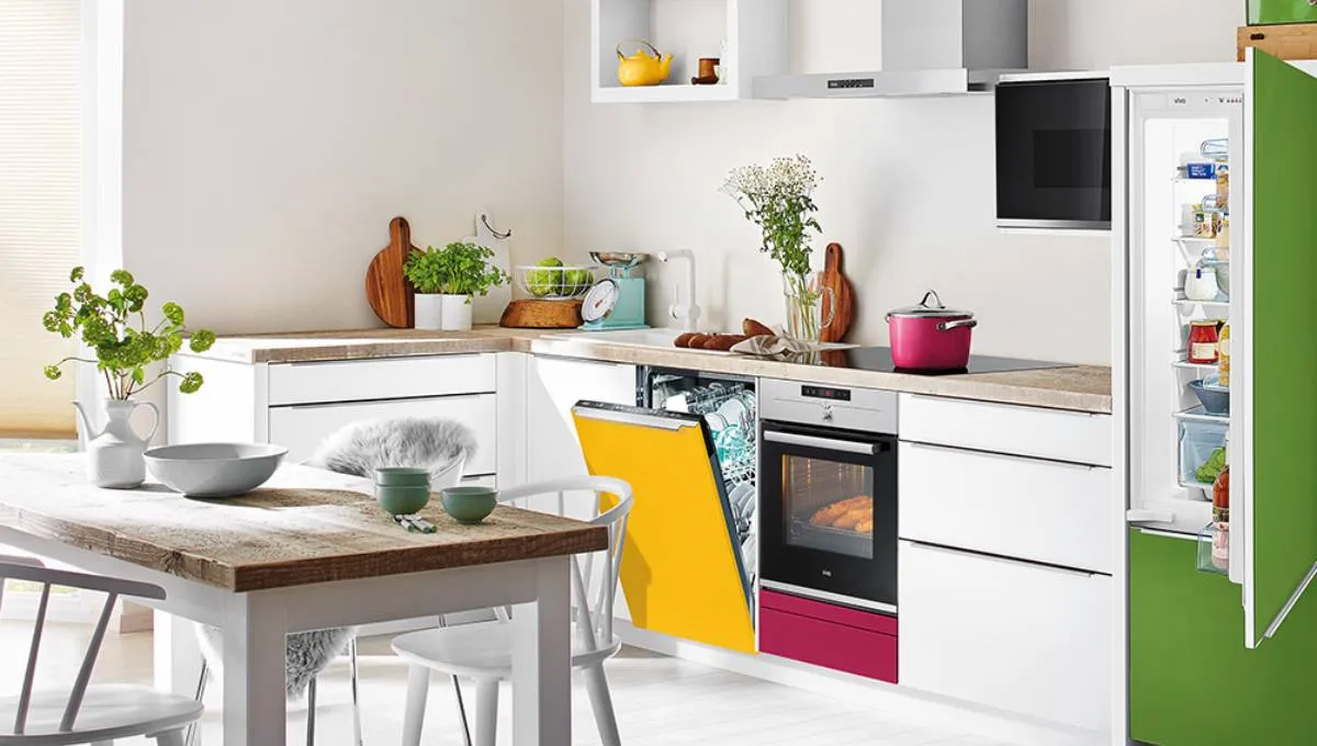 Cuisine moderne et lumineuse avec des placards blancs, des appareils électroménagers colorés — dont un réfrigérateur vert, un lave-vaisselle jaune et un tiroir de four rose — ainsi qu'une table à manger en bois.