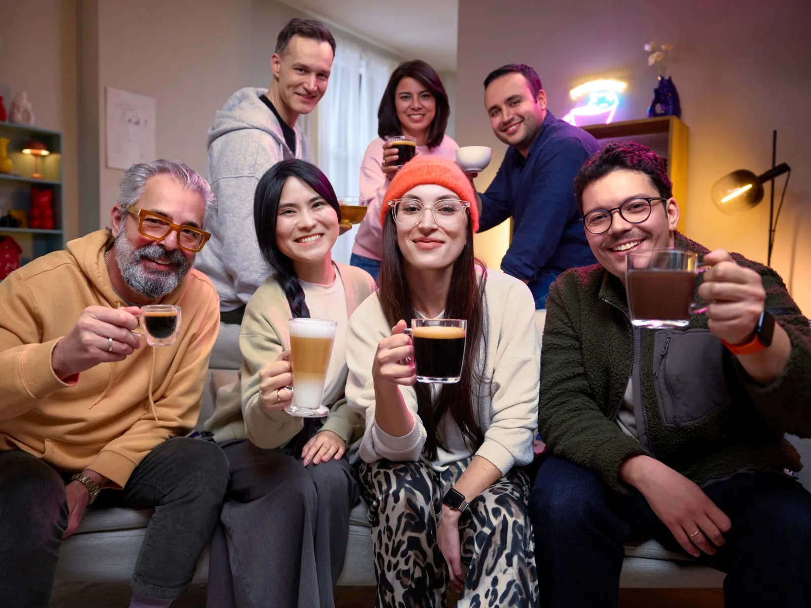 Group of friends and family on a sofa at home, each holding different hot drinks made with the Bosch TASSIMO Harmony coffee machine