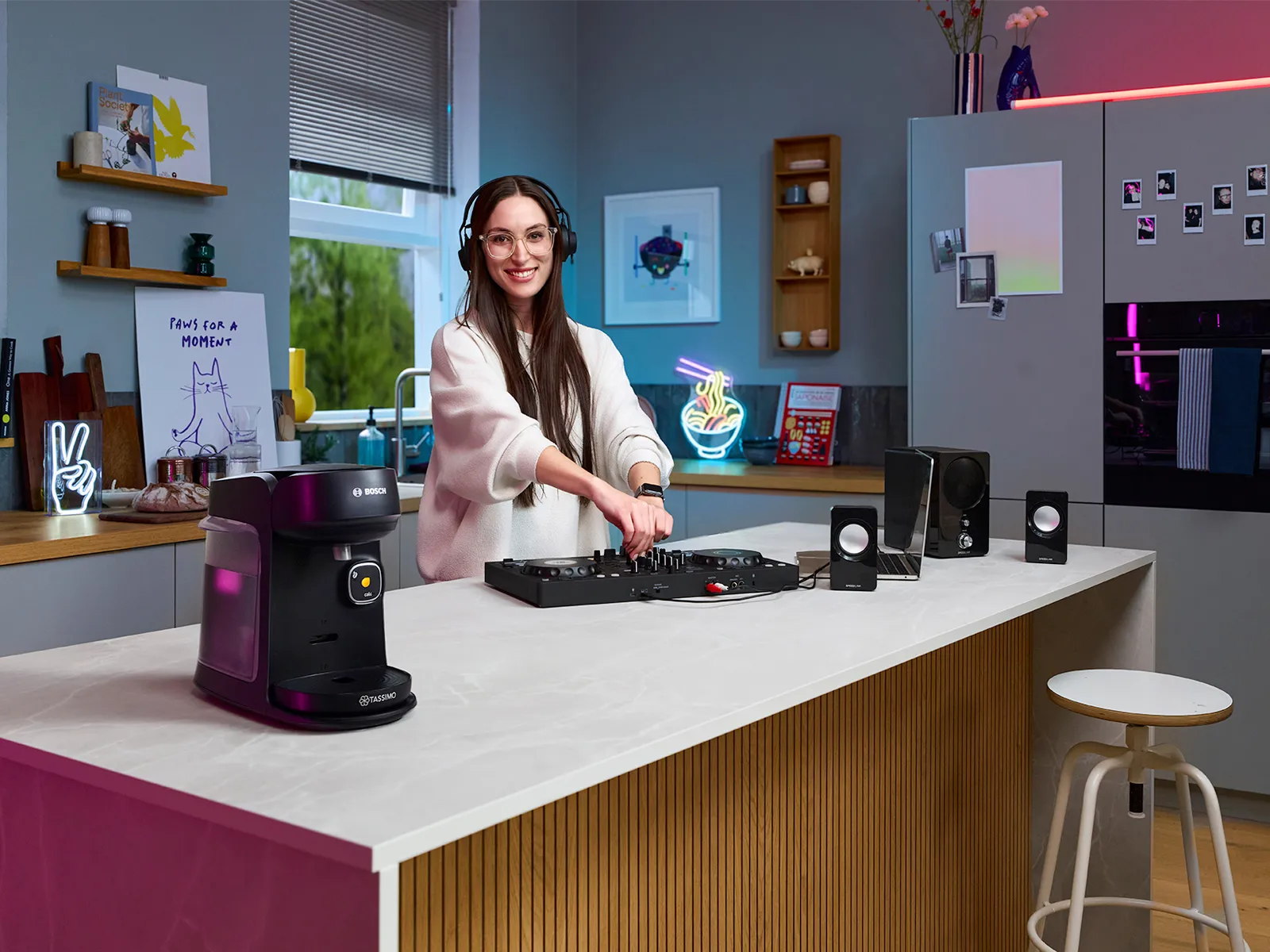 A woman DJ'ing in the kitchen on the counter, with a TASSIMO Harmony coffee machine on the counter as well