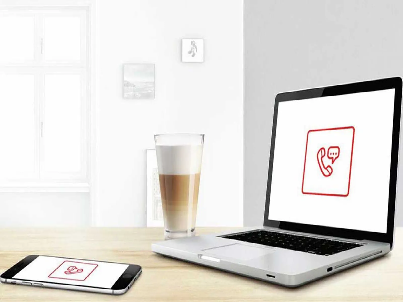 Laptop och smartphone visar samtalsikoner på träbord med kaffekopp.