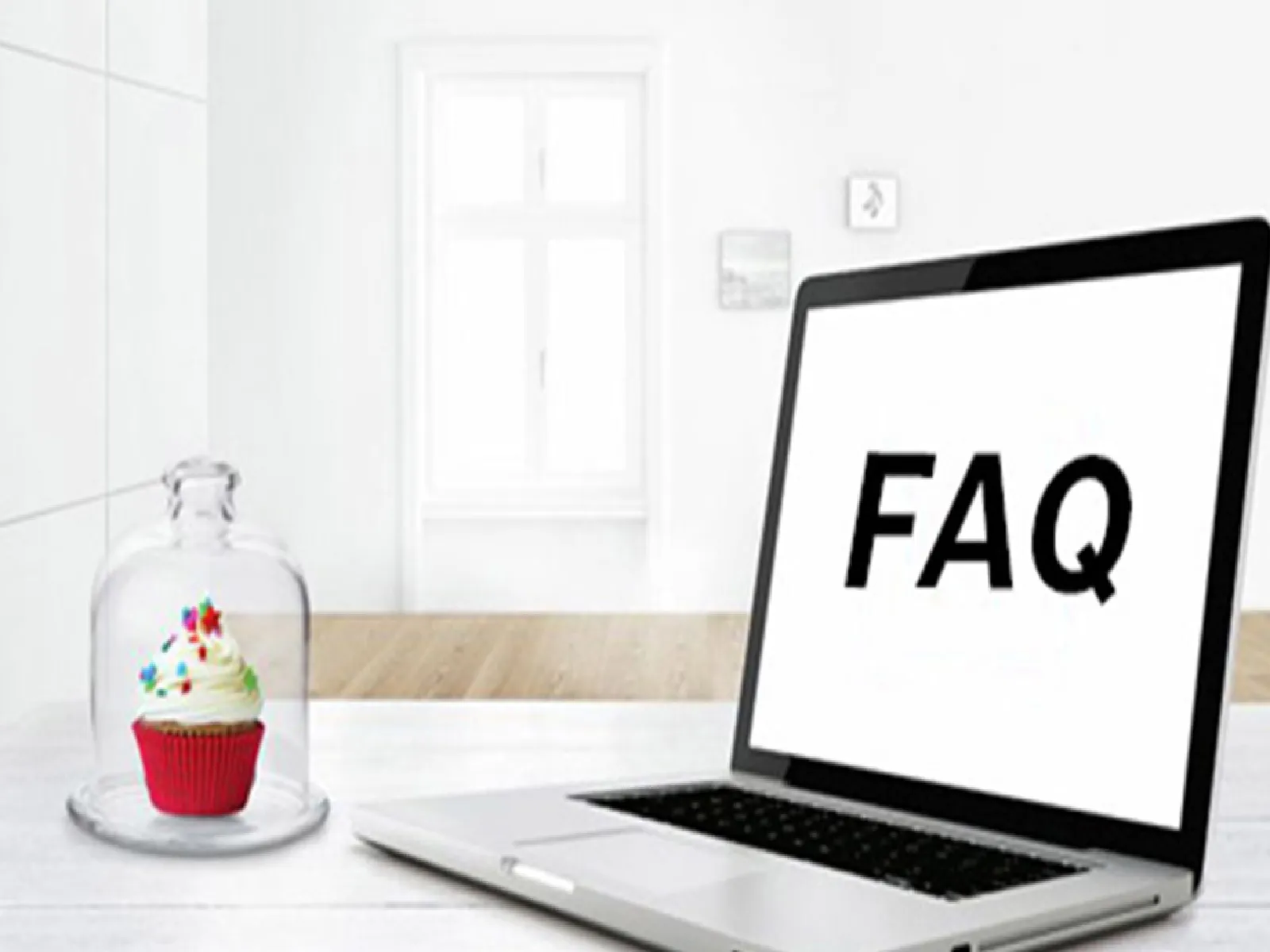 En bärbar dator med "FAQ" på skärmen står på ett vitt skrivbord bredvid en ensam cupcake under en glaskupol i ett ljust, minimalistiskt rum.