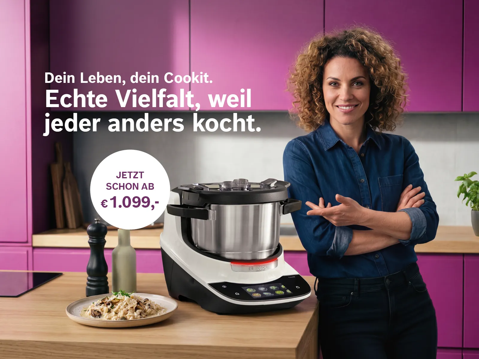 Lächelnde Frau im blauen Hemd neben einem Bosch Cookit (Küchenmaschine mit Kochfunktion) auf einer Holzarbeitsplatte. Im Hintergrund eine moderne Küche mit lila Schränken und frischem Basilikum. Links steht der Text 'Dein Leben, dein Cookit. Echte Vielfalt, weil jeder anders kocht.' sowie ein Preishinweis 'Jetzt schon ab € 1.099,-'.