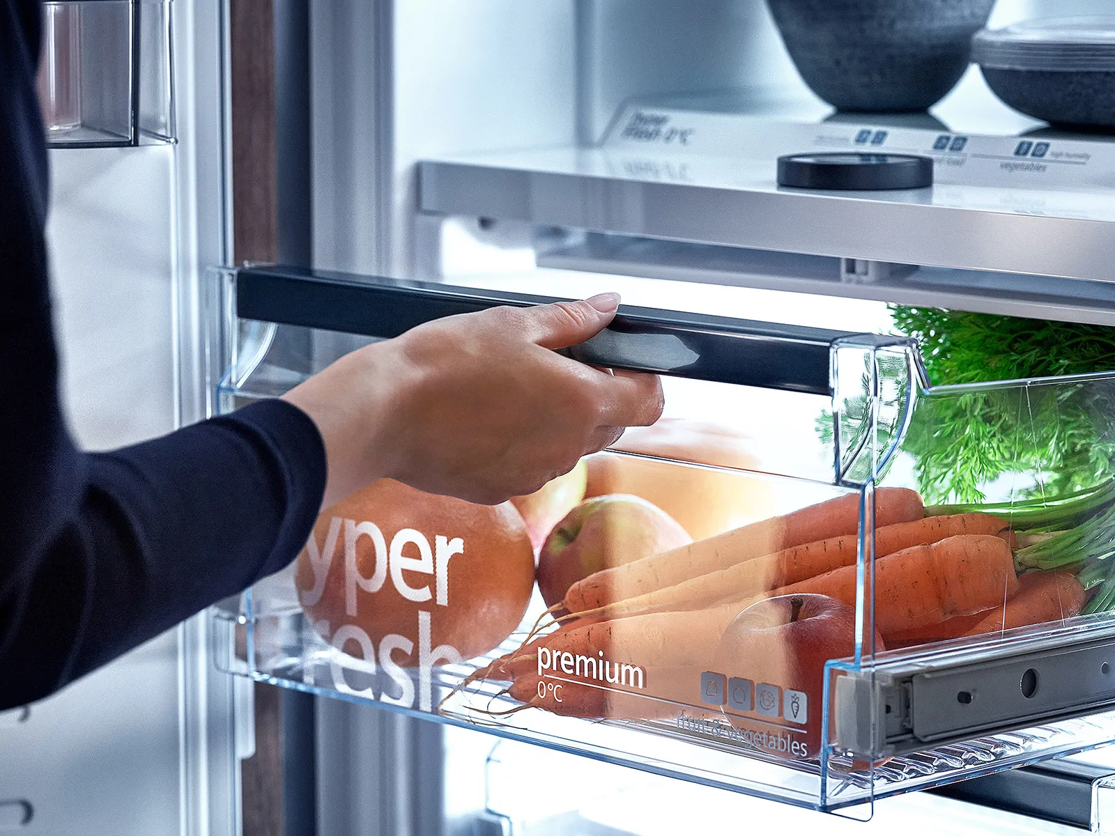 Mano che si allunga all'interno di un frigorifero aperto, ben rifornito di vari alimenti tra cui pane, verdure e un prodotto a marchio Tyson.